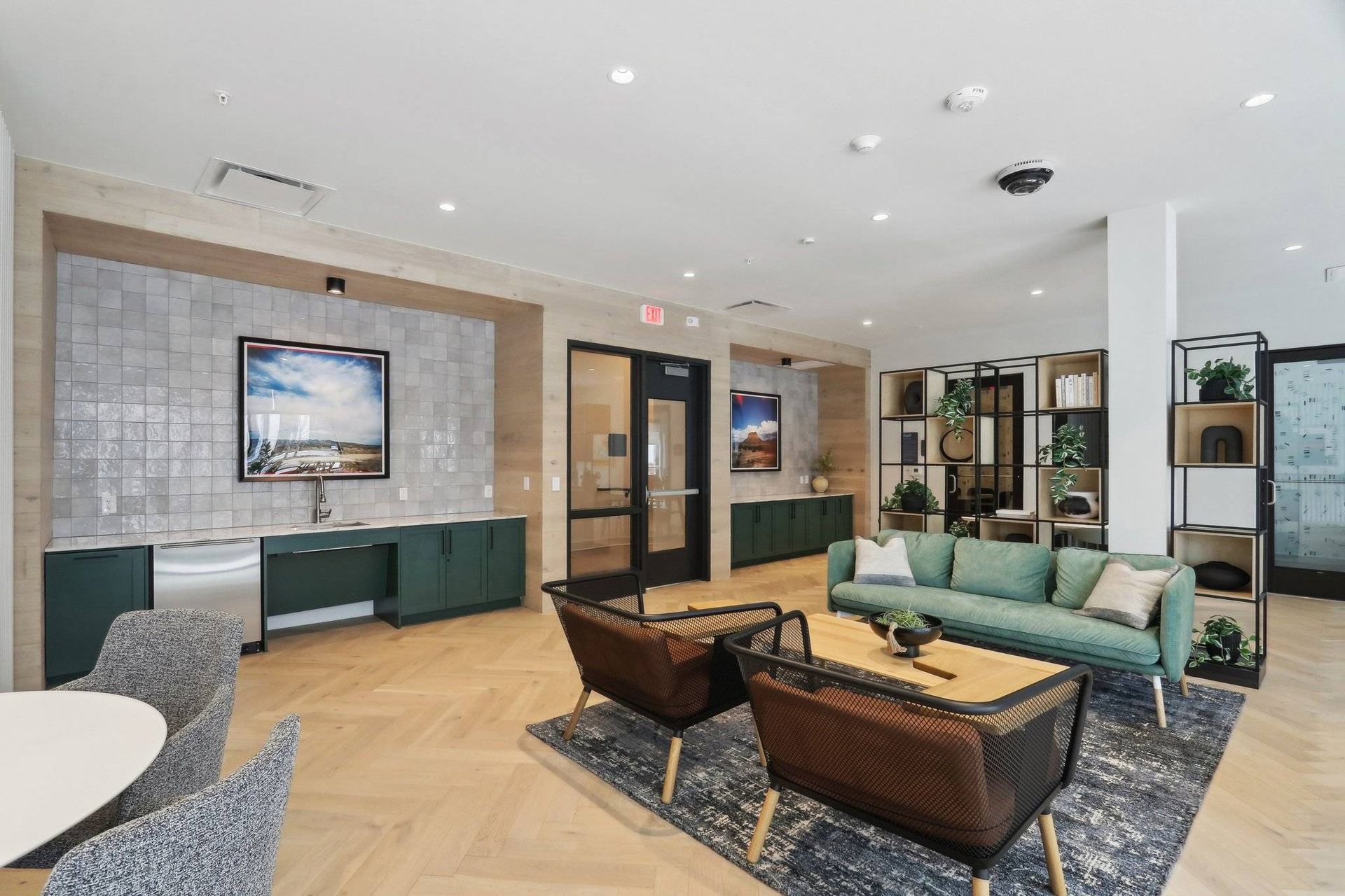 Contemporary apartment community lounge with seating, shelves, and a kitchenette.