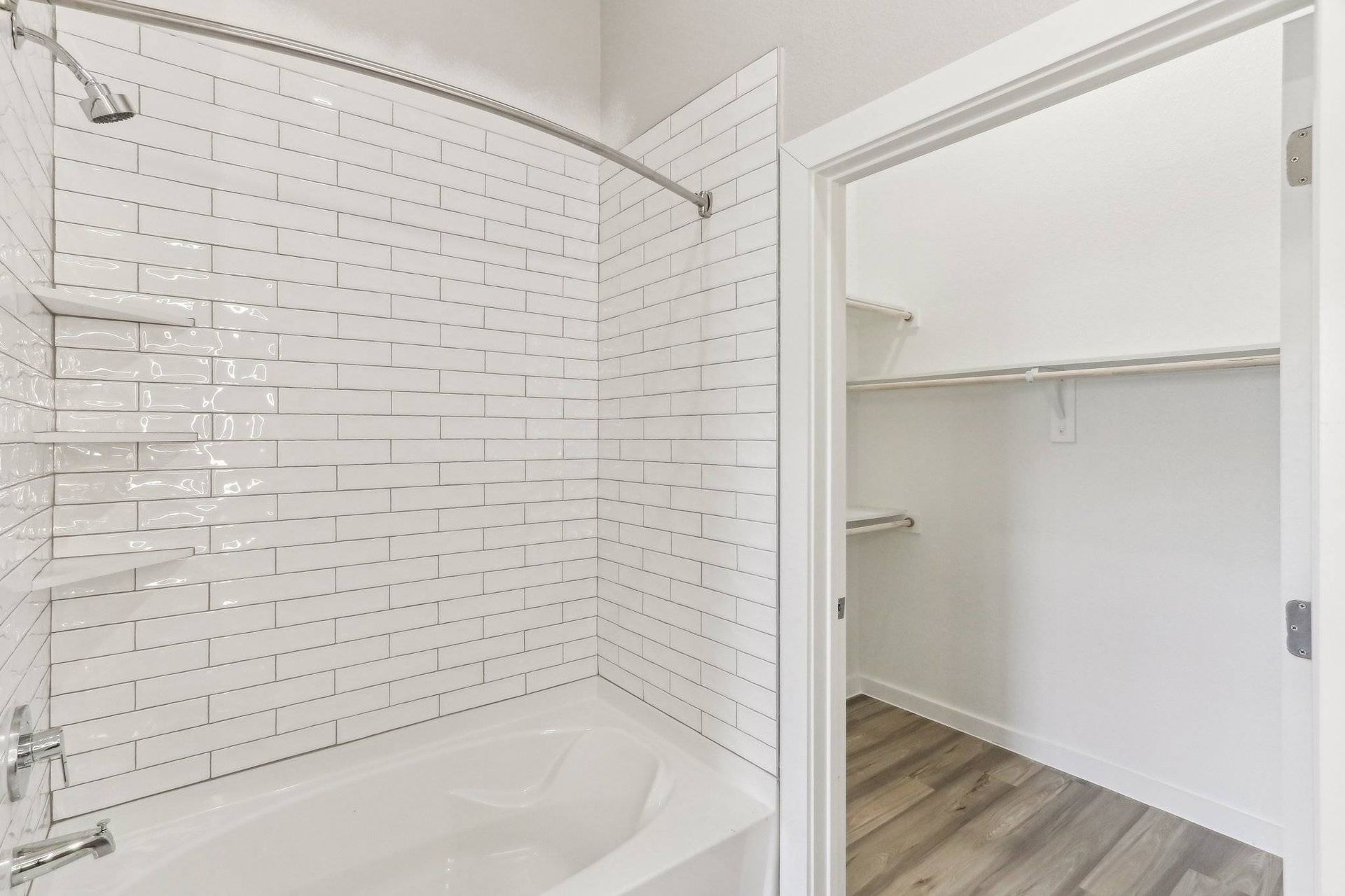 Bathroom with white subway tile walls, a tub/shower combo, and a closet with shelves and a hanging rod.