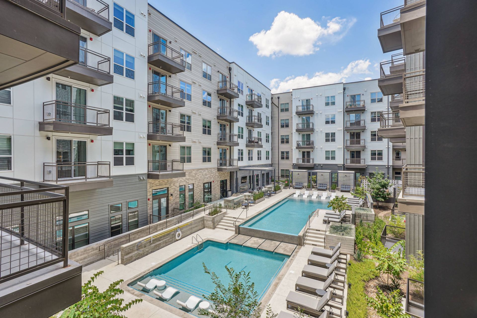 Outdoor courtyard with two pools, lounge chairs, and surrounding apartment balconies.