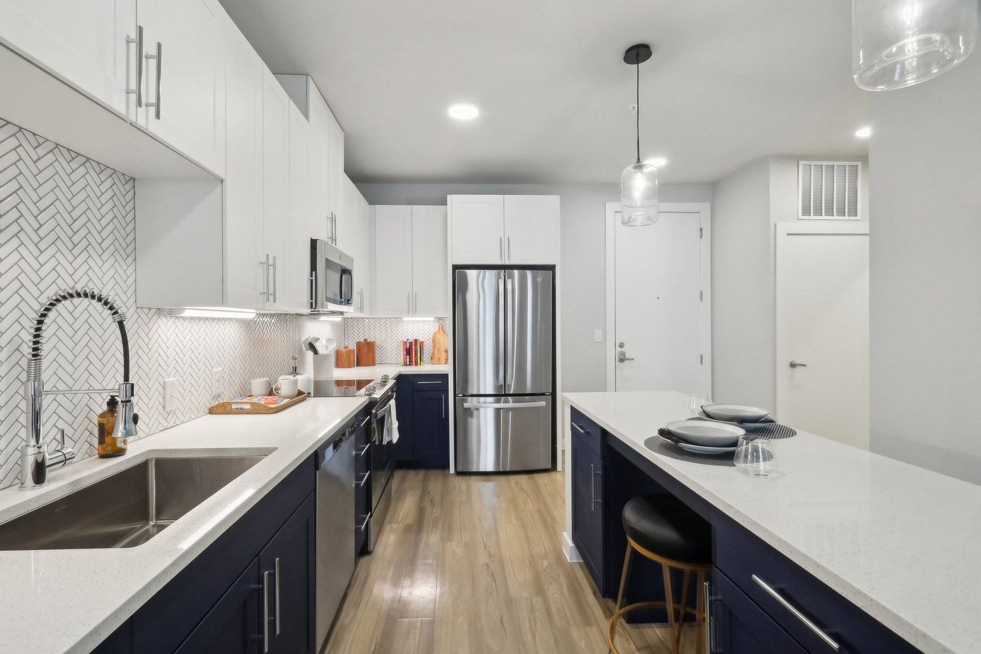 Modern kitchen with white upper cabinets, navy lower cabinets, stainless steel appliances, and a large island.