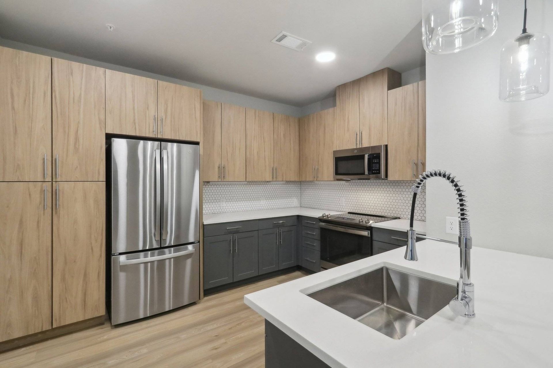 Modern kitchen with stainless steel appliances, light wood upper cabinets, and an island sink.