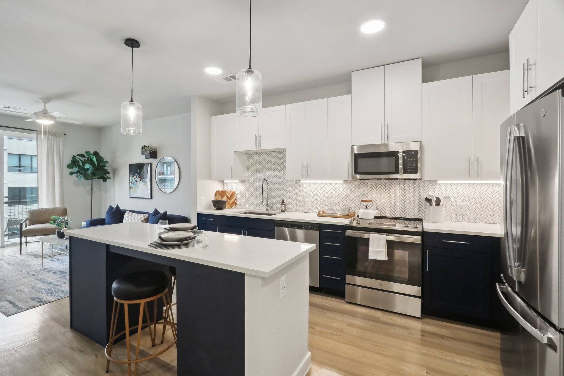 Open-concept kitchen with white upper cabinets, navy lower cabinets, and stainless steel appliances.