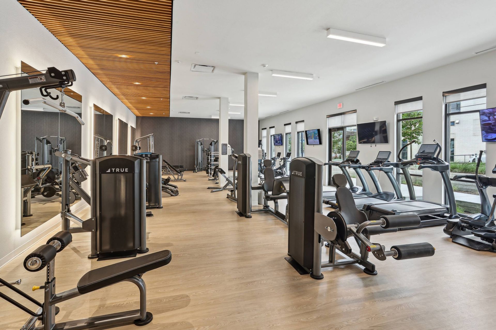 Well-lit gym with cardio machines, weight stations, and workout benches.