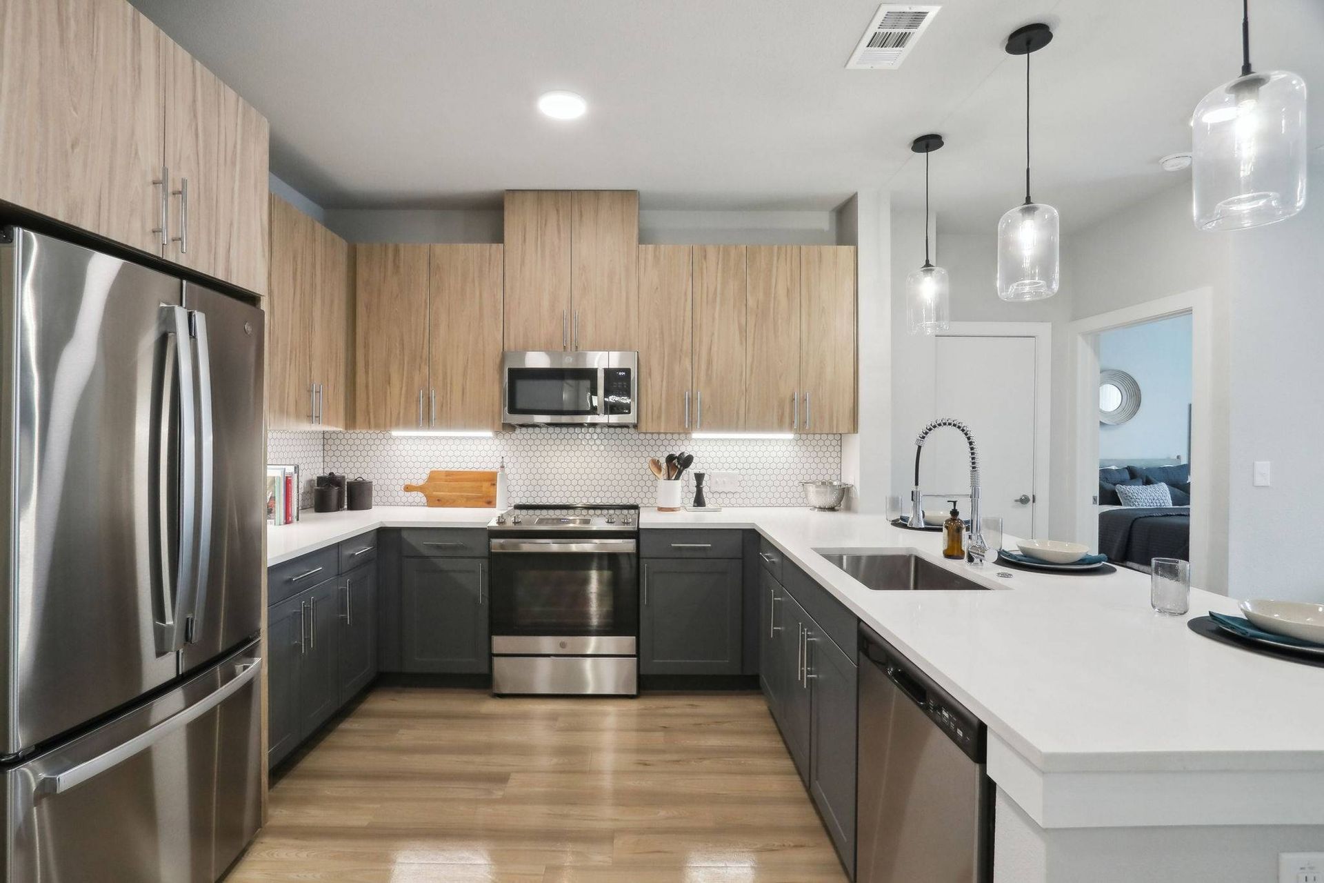 Modern kitchen with light wood upper cabinets, dark gray lower cabinets, stainless appliances, and island with sink.