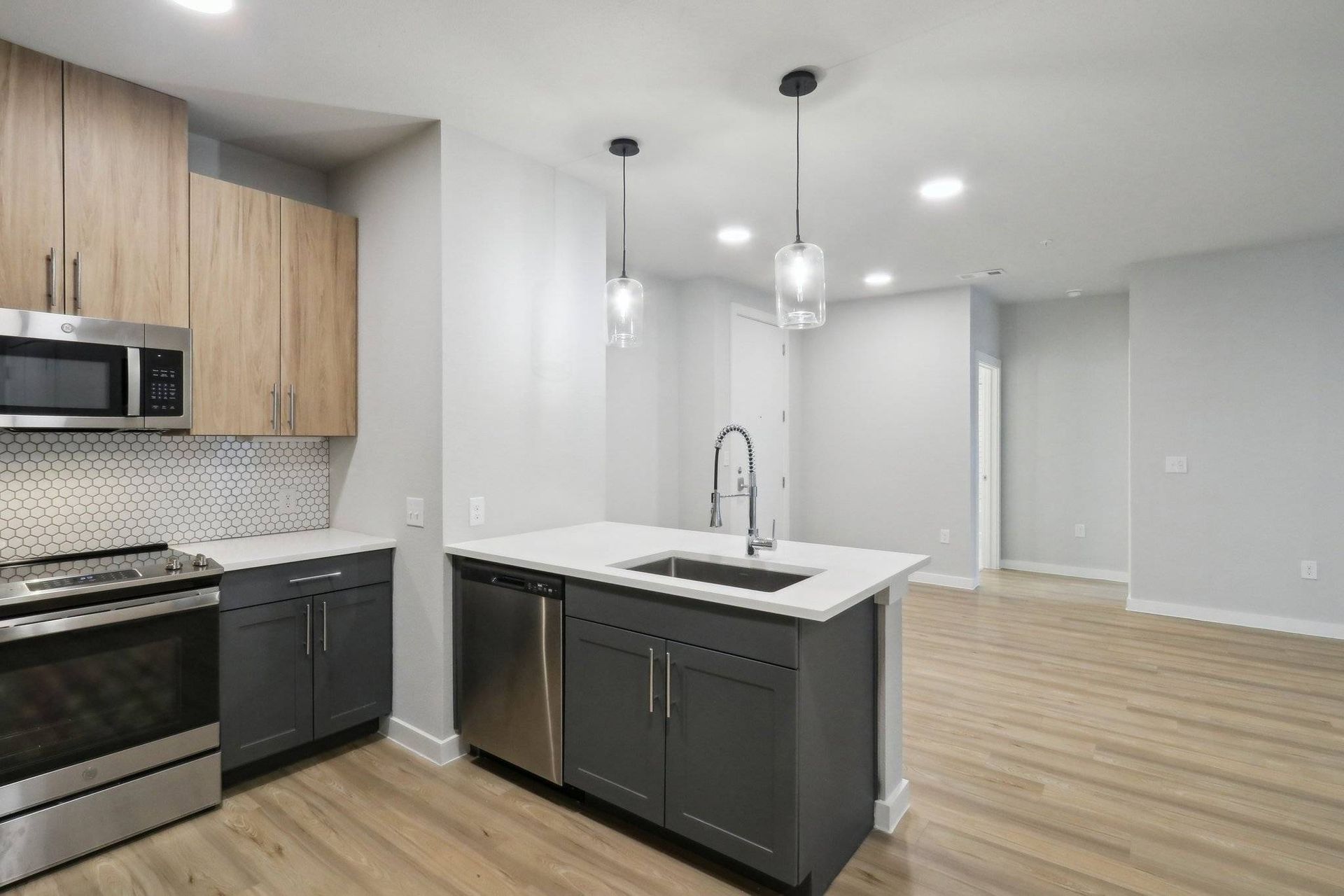 Open-concept kitchen in a modern apartment with an island, stainless steel appliances, and light wood cabinets.