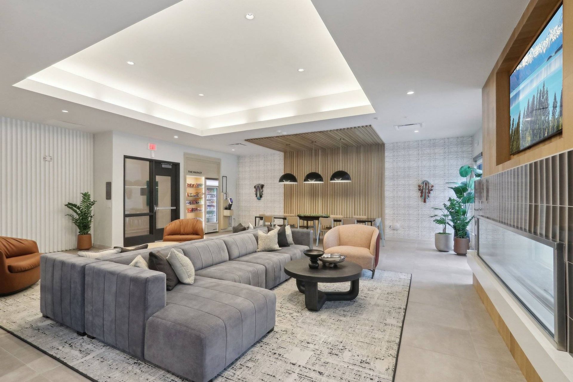 Modern apartment community lounge with a large gray sectional, coffee table, and plants.