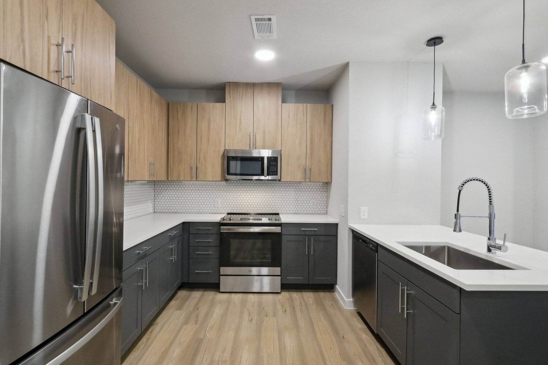 Modern kitchen with stainless steel appliances, light wood upper cabinets, and dark gray lower cabinets.
