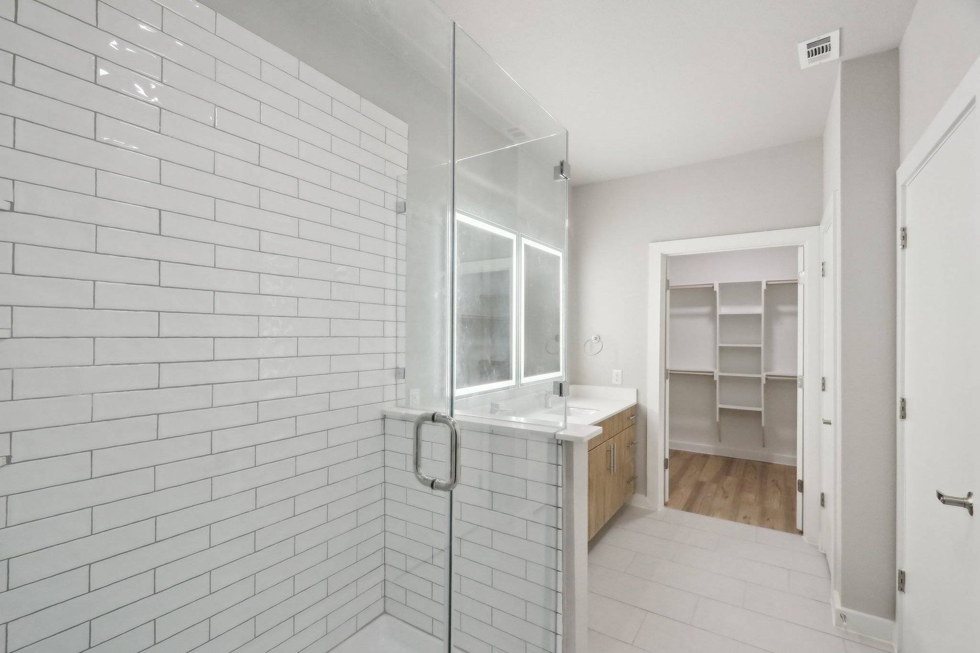 Glass-enclosed shower with white subway tile and a light wood vanity.