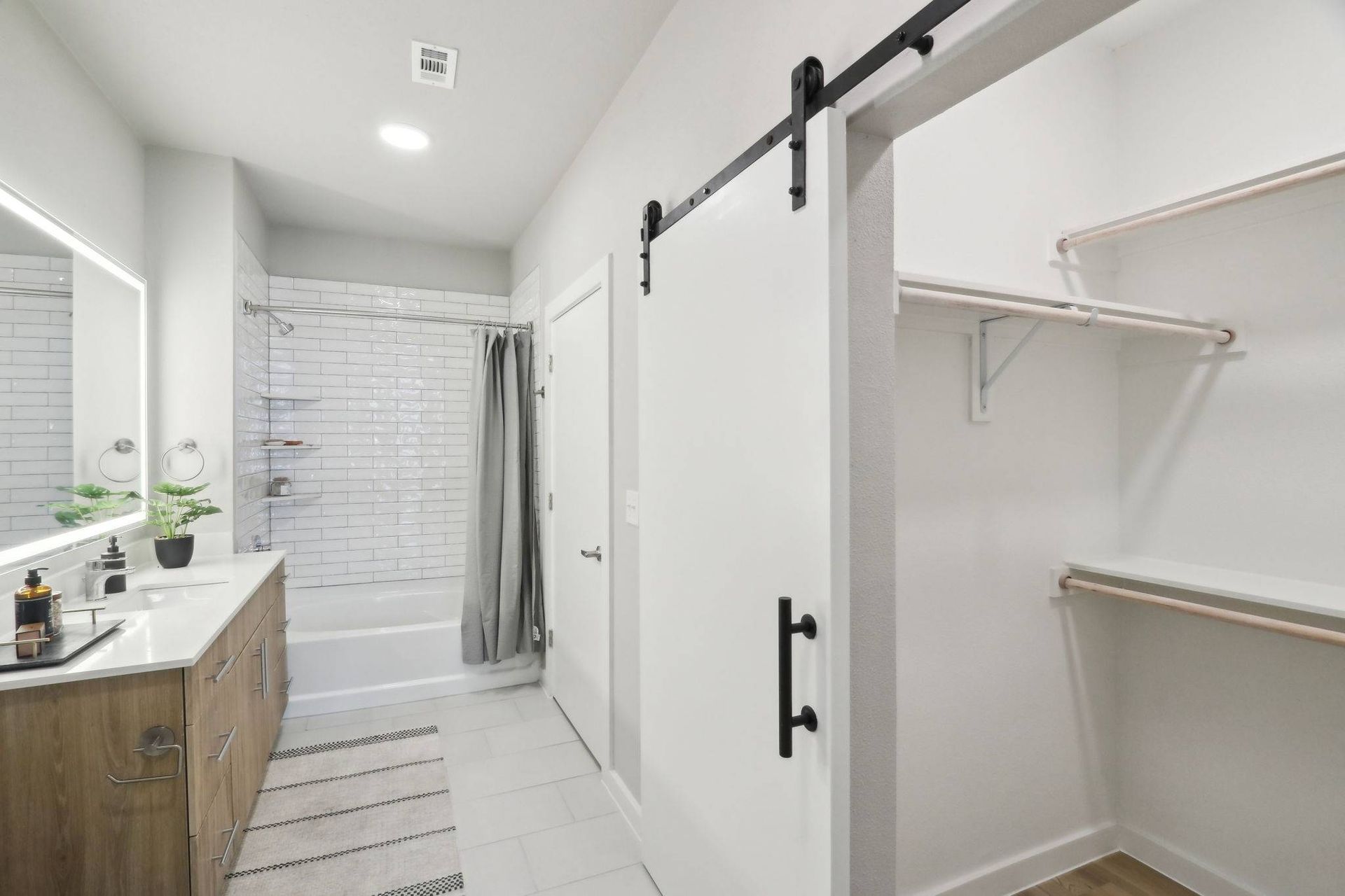Modern bathroom with double vanity, white subway-tile tub/shower, and adjacent closet with hanging rods.