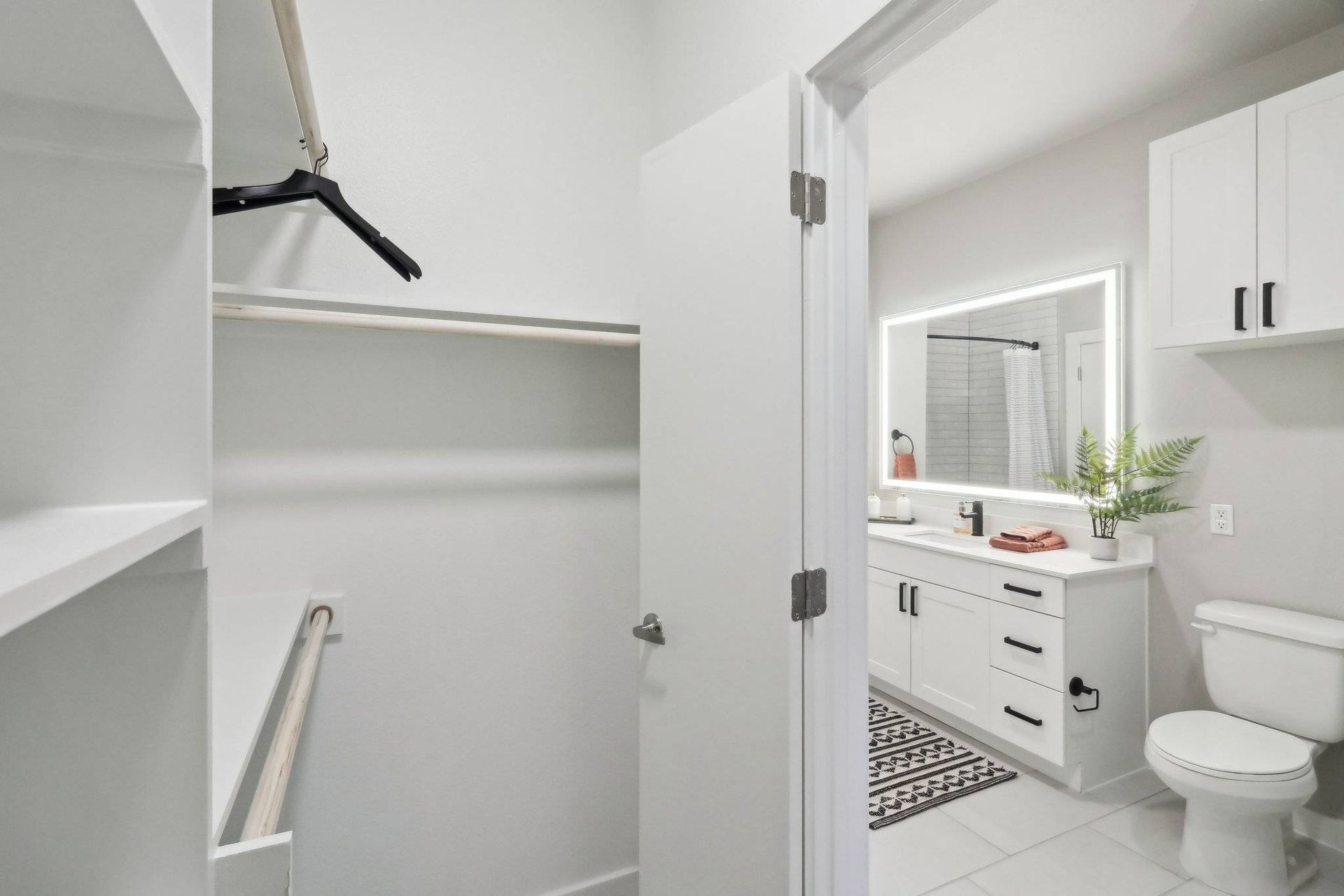 Bright modern bathroom with white vanity, backlit mirror, and a connected walk-in closet.