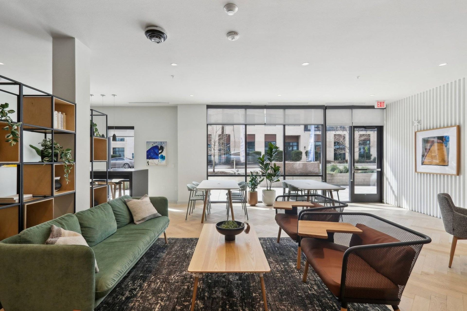 Bright apartment lobby with a green sofa, chairs, plants, and large windows.
