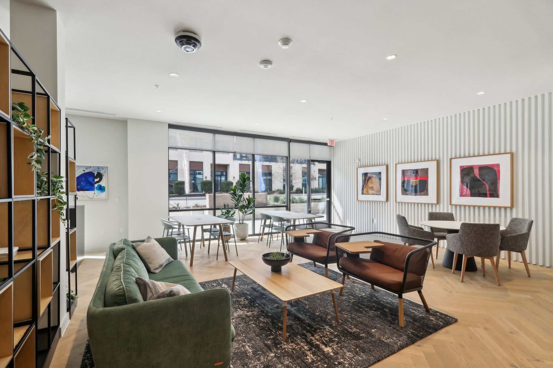 Modern lounge area with green sofa, art, tables, and outdoor patio view.