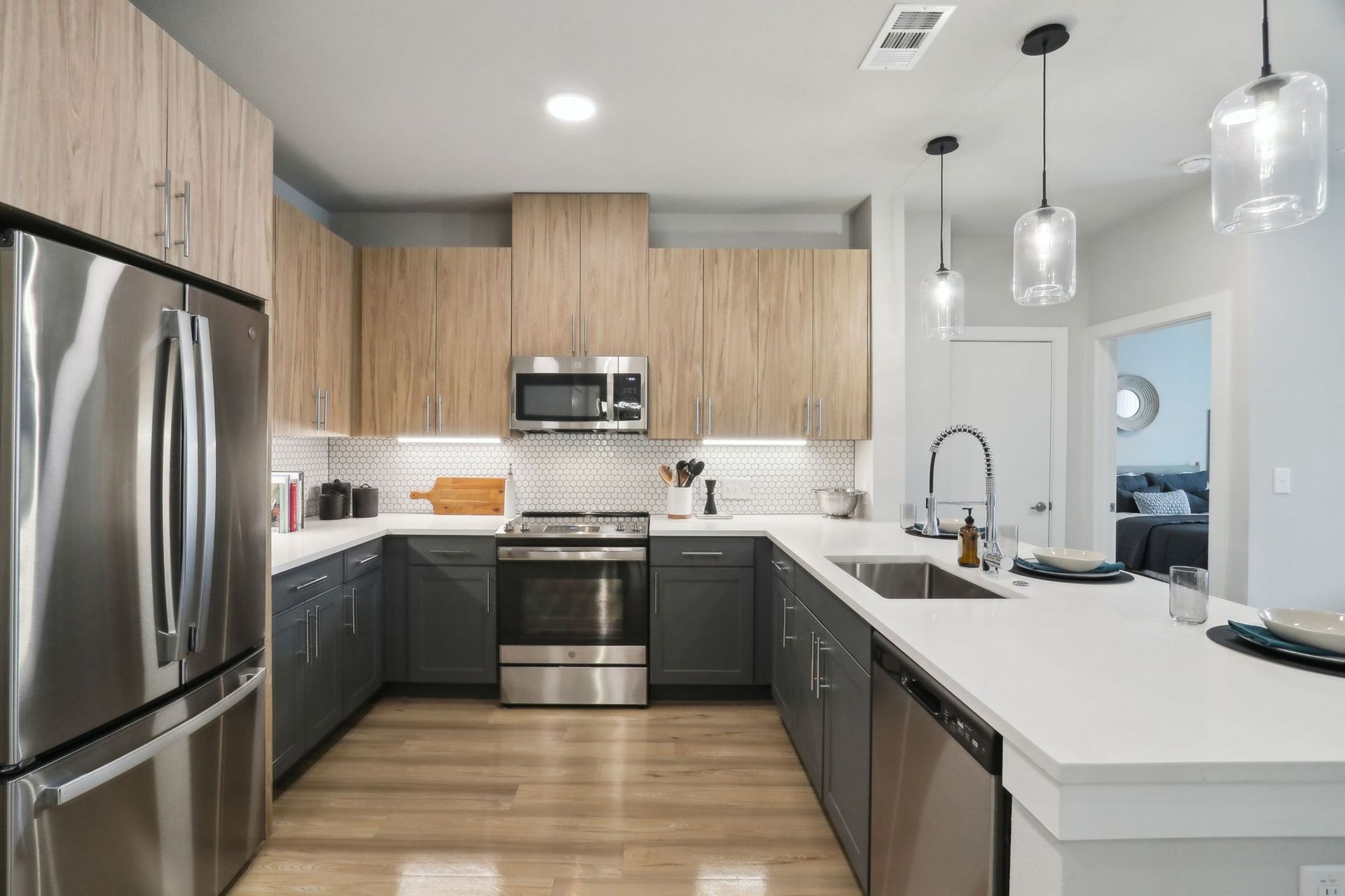 Modern U-shaped kitchen with stainless steel appliances, light wood cabinets, and gray lowers.