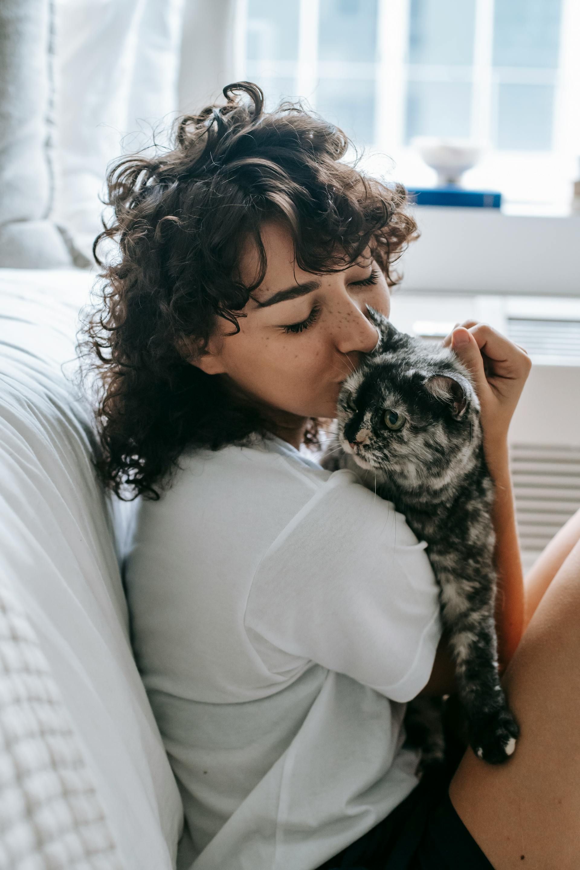 Pregnant person petting a cat, sitting next to a person using a laptop on a sofa.