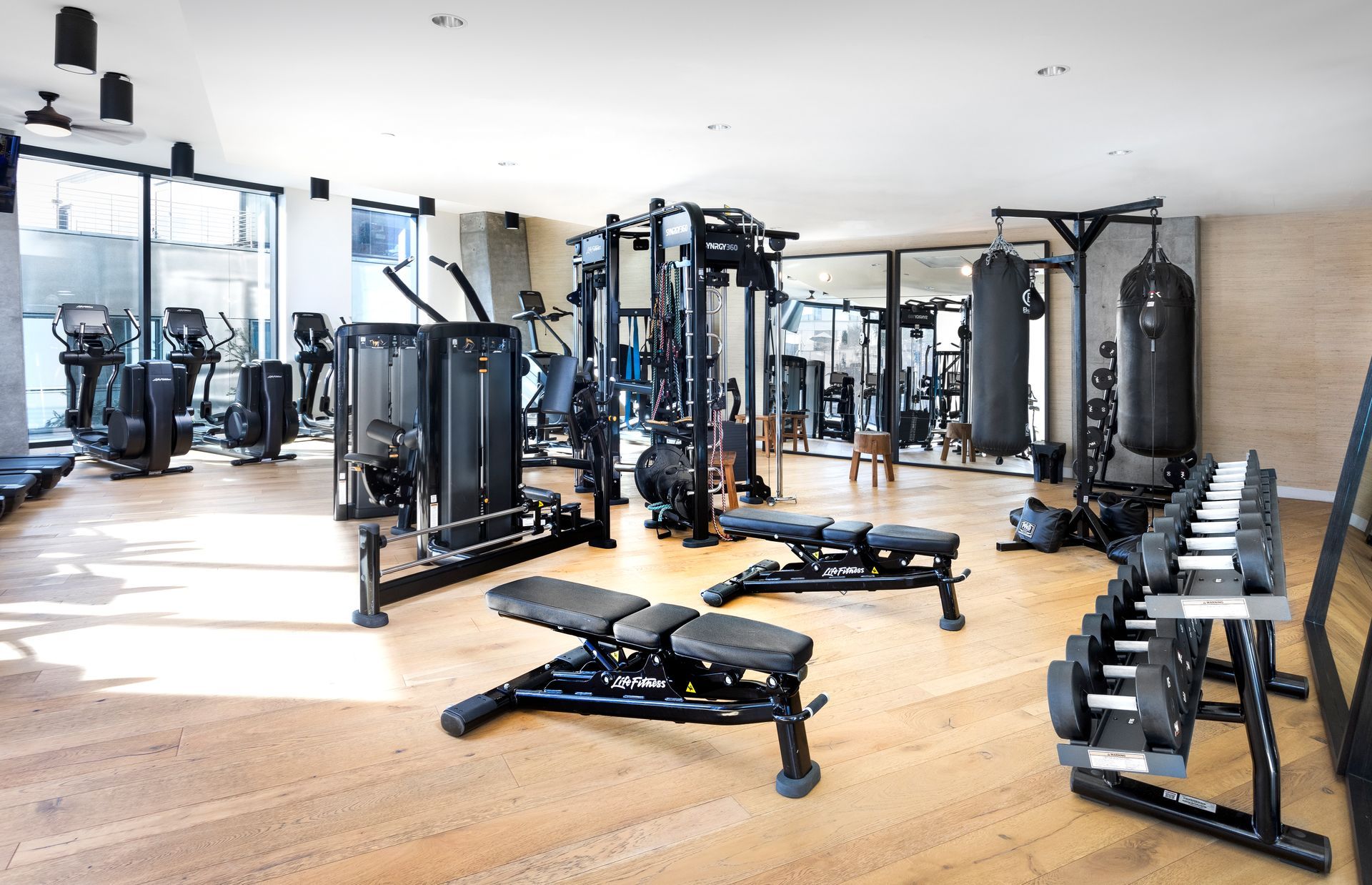 Modern gym with weight machines, benches, dumbbells, and wood flooring