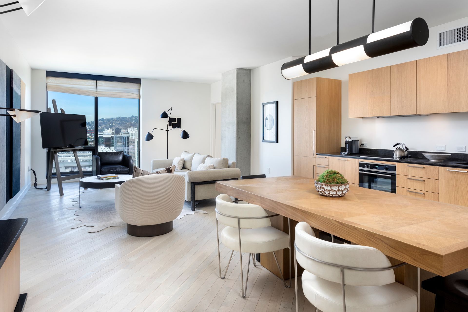 Modern open-plan kitchen and living room with wood island, white furniture, and city-view windows