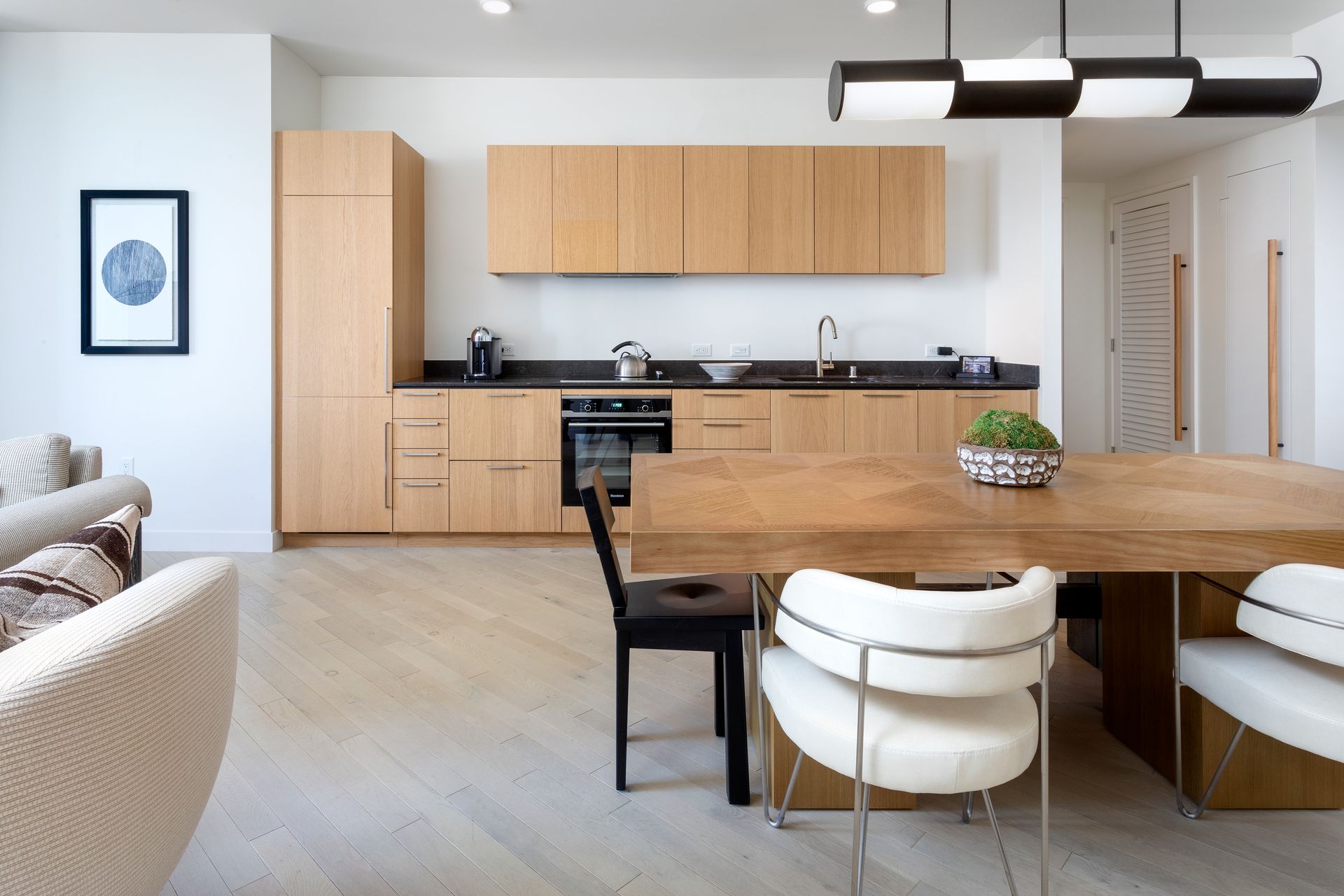 Bright modern kitchen and dining area with light wood cabinets, wooden table, and white chairs.