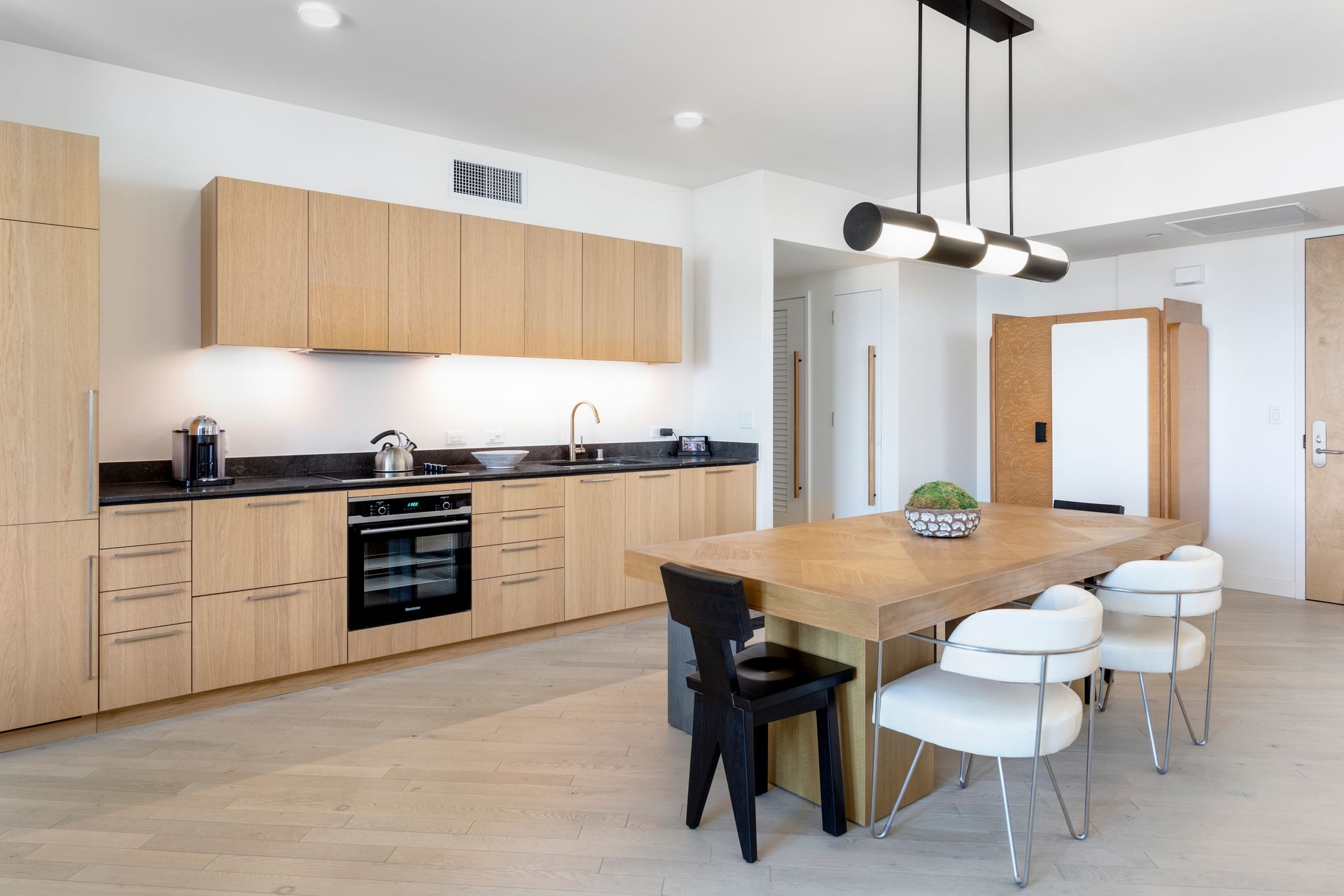 Modern kitchen with light wood cabinets, large island, pendant lights, and white bar stools
