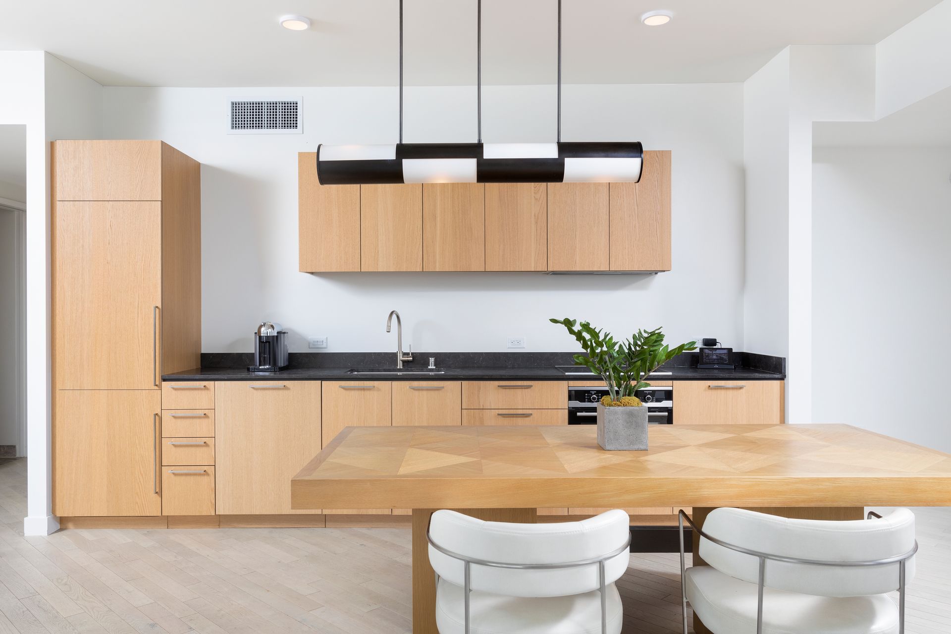 Modern kitchen with light wood cabinets, black countertops, and a dining table in the foreground