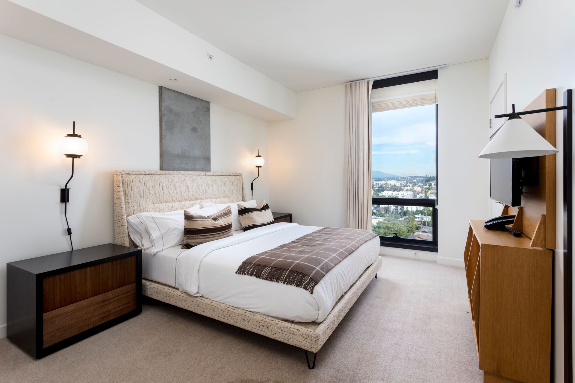 Modern bedroom with a bed, nightstands, and a floor-to-ceiling window overlooking the city.