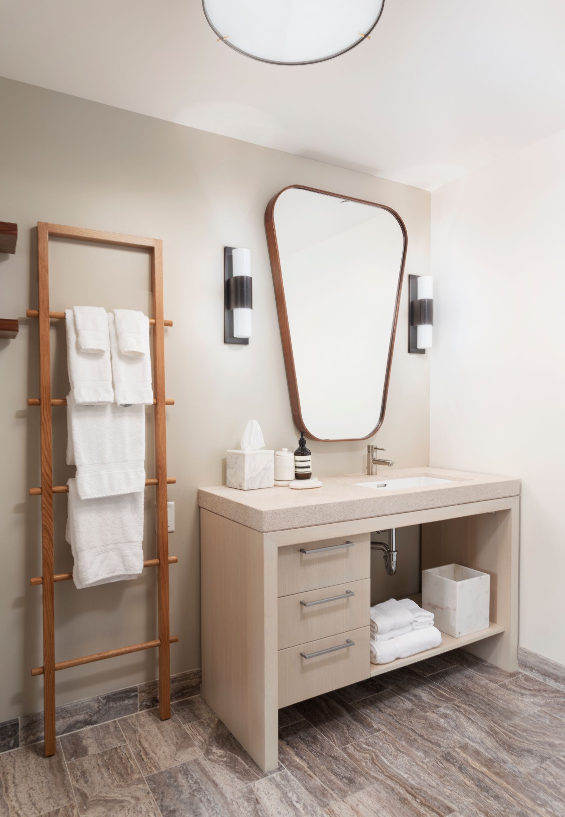 Modern bathroom vanity with mirror, wall sconces, towel ladder, and neatly folded towels