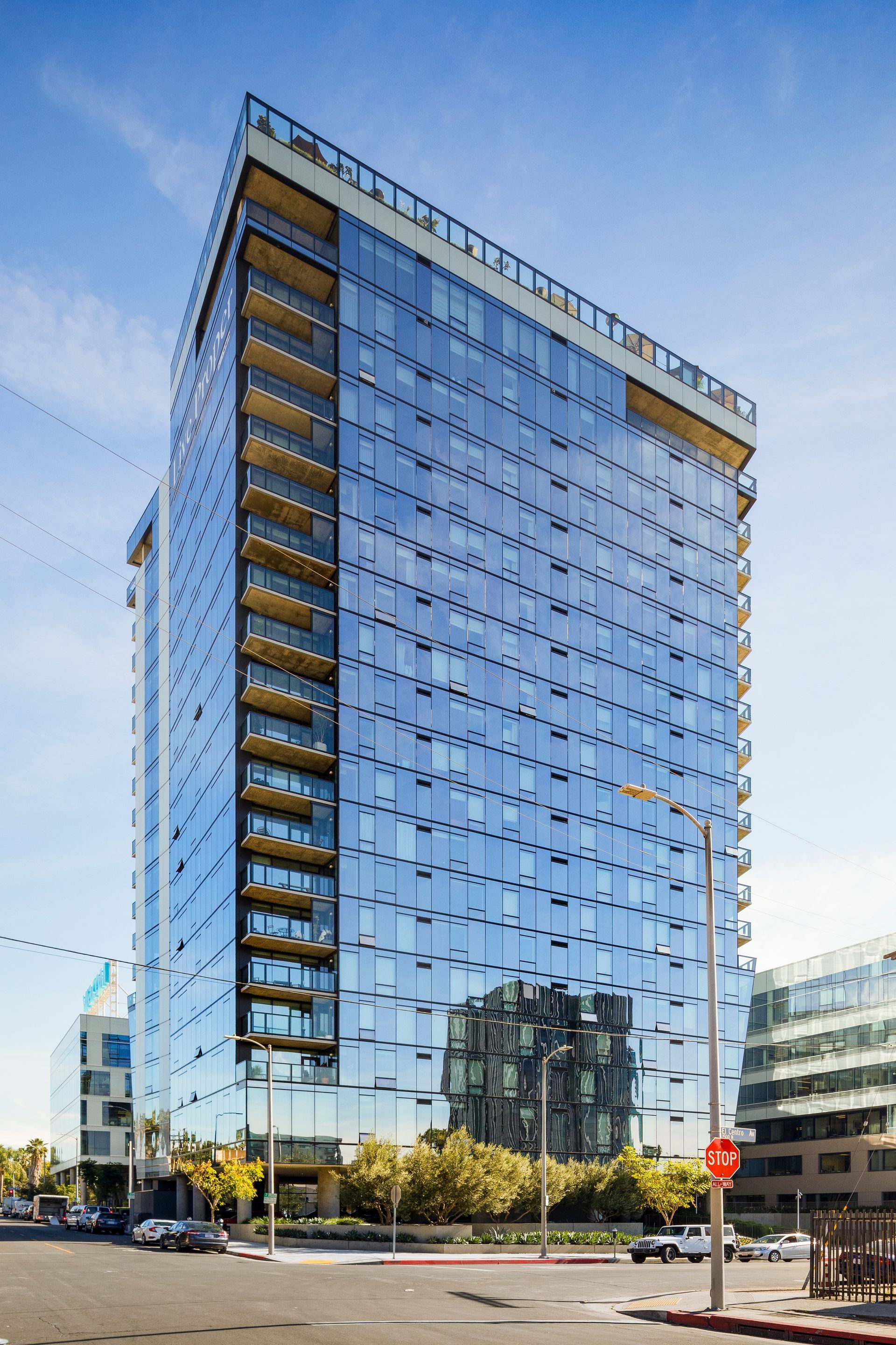 Glass office tower with blue-tinted windows beside a city street on a clear day