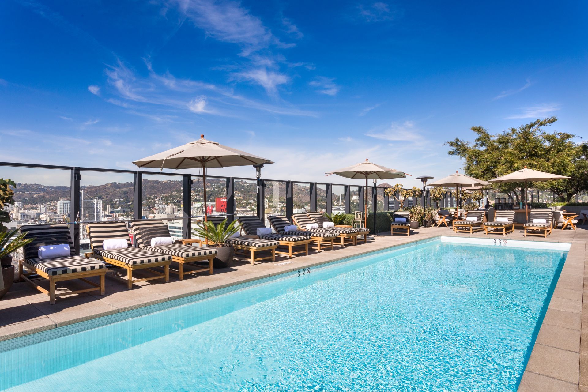 Rooftop pool with lounge chairs, umbrellas, and city skyline under a blue sky