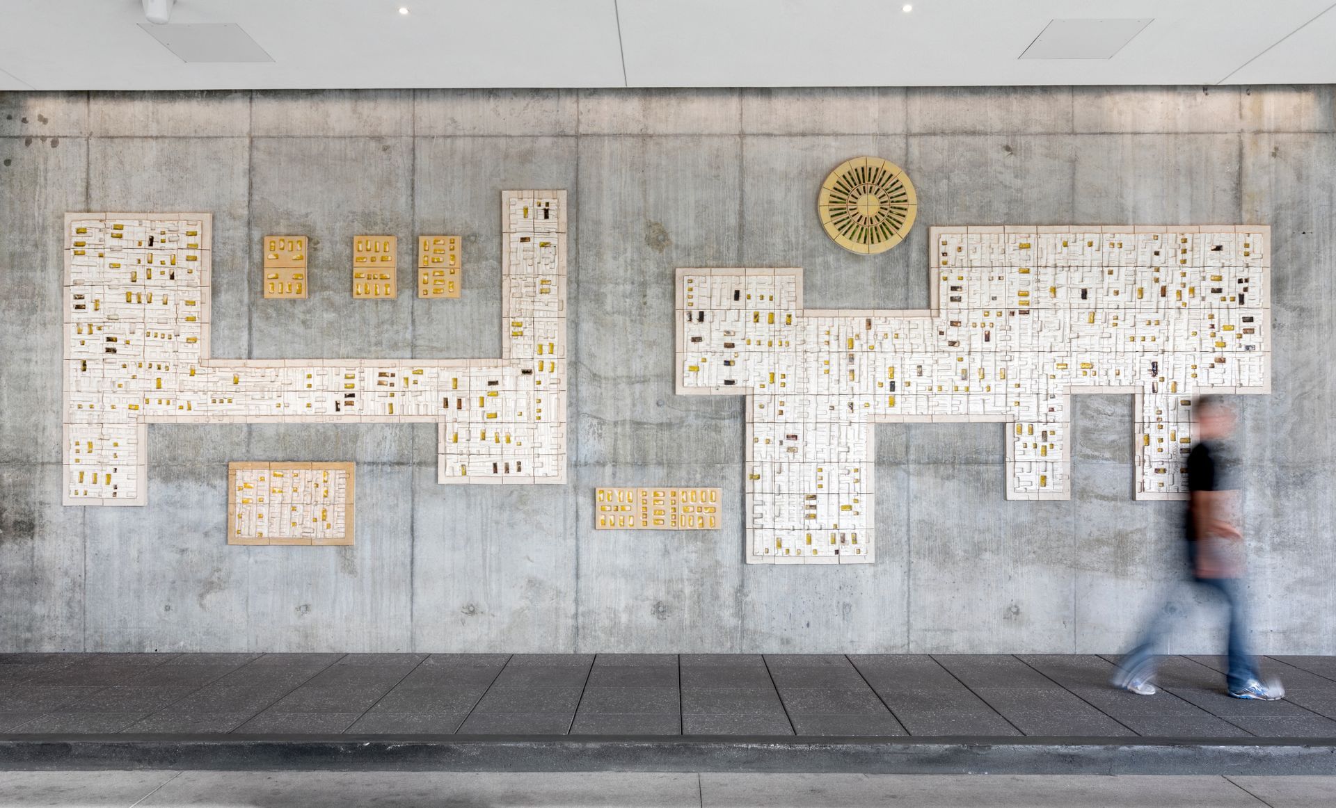 Long concrete wall covered with white and yellow maps; blurred person walking past on sidewalk.
