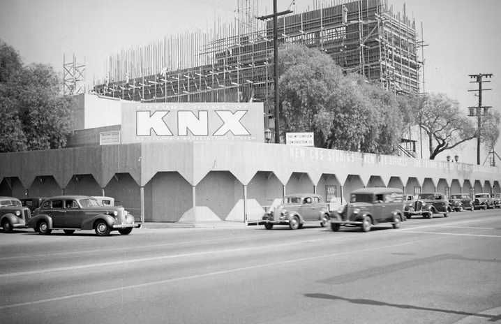 Black-and-white street view of KNX building under construction, with cars parked along the road.