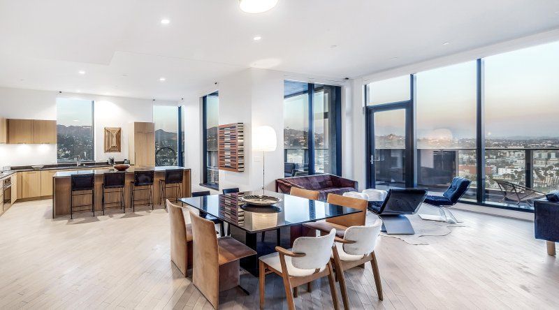Modern open-plan apartment with kitchen island, dining table, lounge chairs, and large city-view windows
