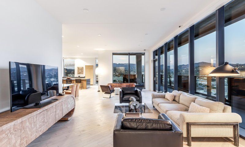 Modern open-plan living room with sectional sofa, large TV, and floor-to-ceiling windows overlooking a city view