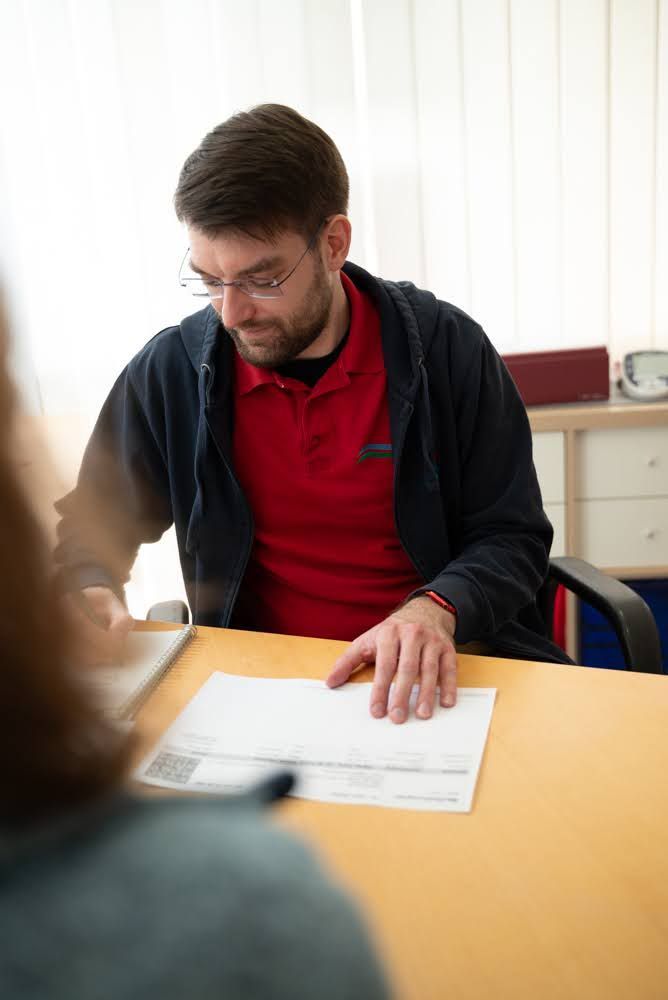 Ein Mann sitzt an einem Tisch und betrachtet ein Blatt Papier.