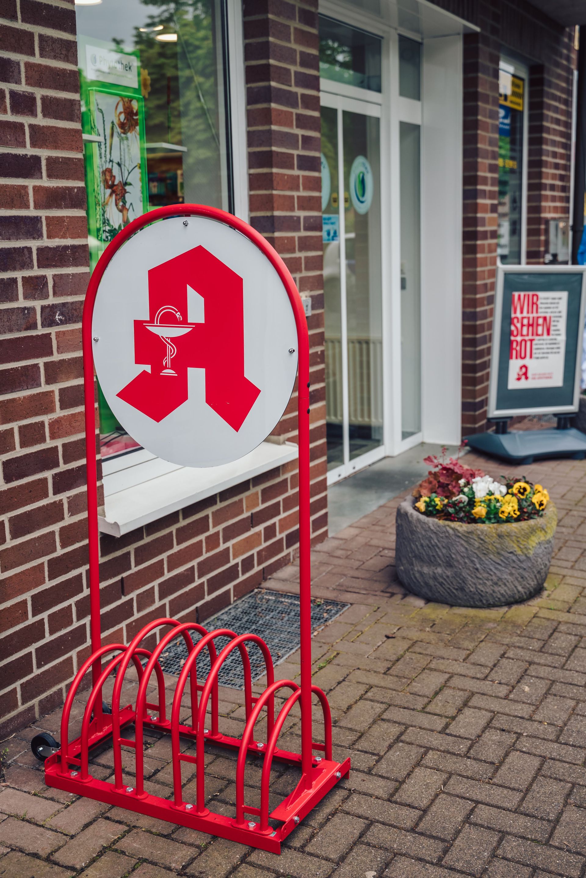 Vor einem Backsteingebäude steht ein roter Fahrradständer.