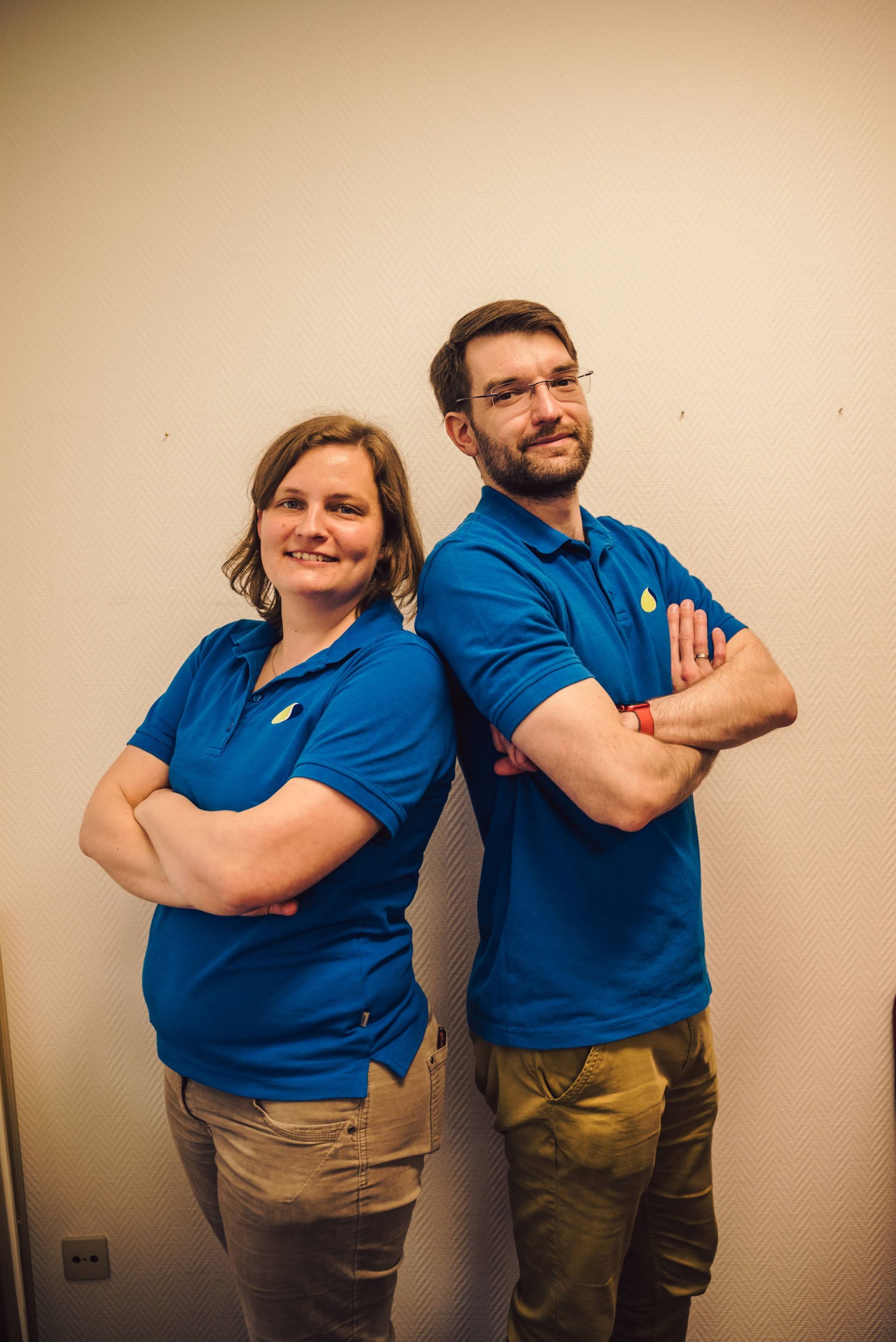 Ein Mann und eine Frau stehen Rücken an Rücken und haben die Arme verschränkt.