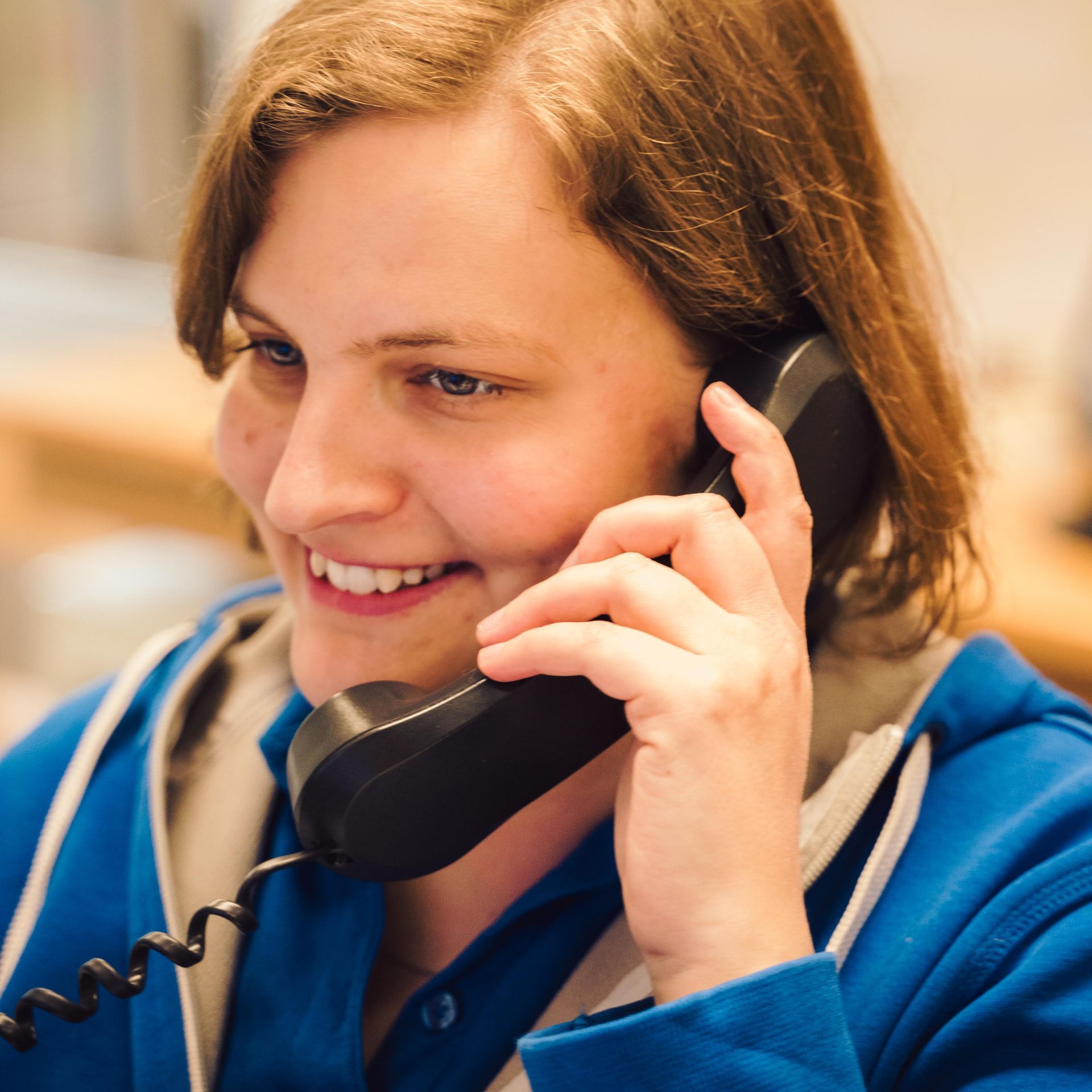Eine Frau in einem blauen Hemd lächelt, während sie telefoniert