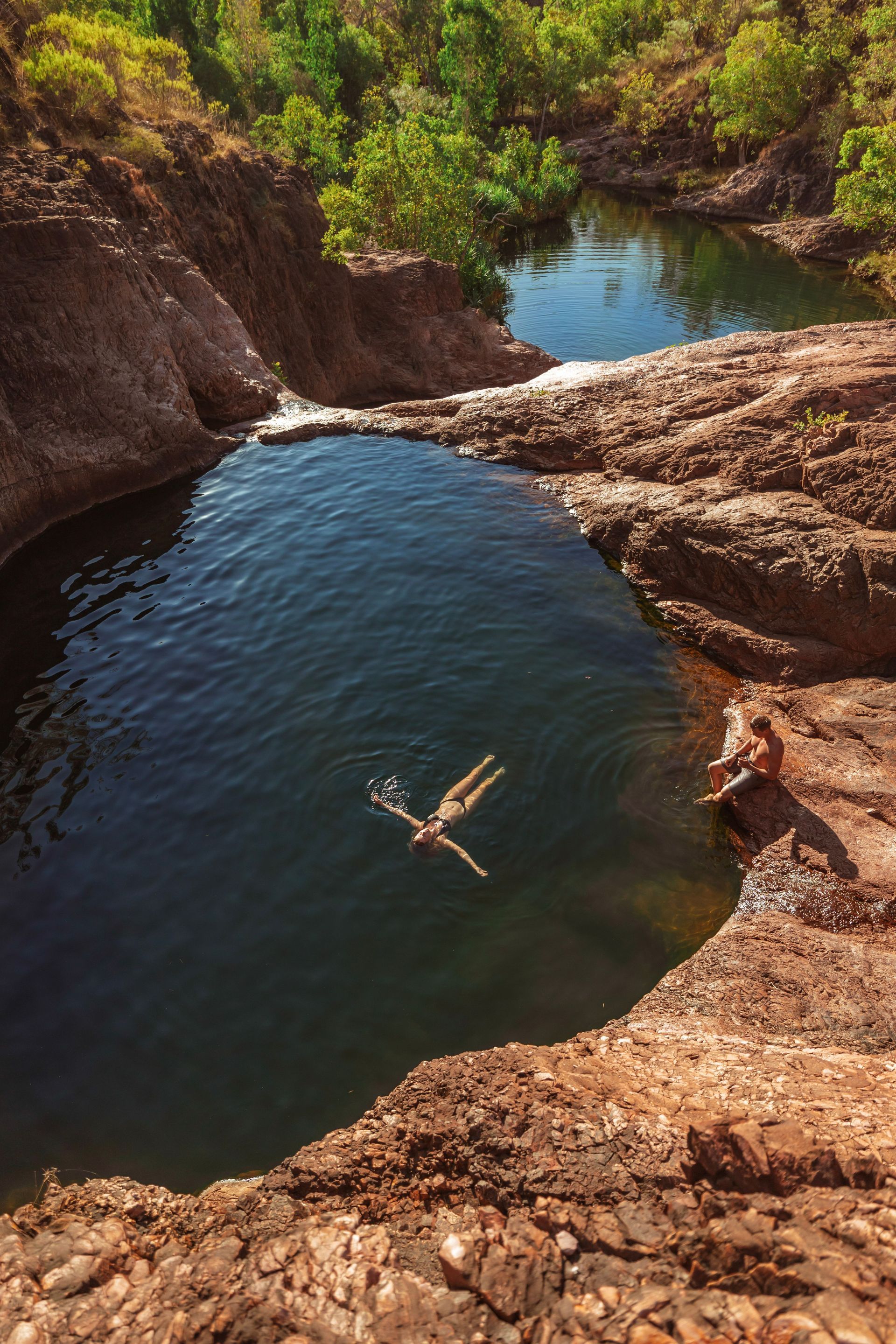 A Person is Swimming in a Small Pond Surrounded by Rocks — Territory Limousine Service in Litchfield, NT