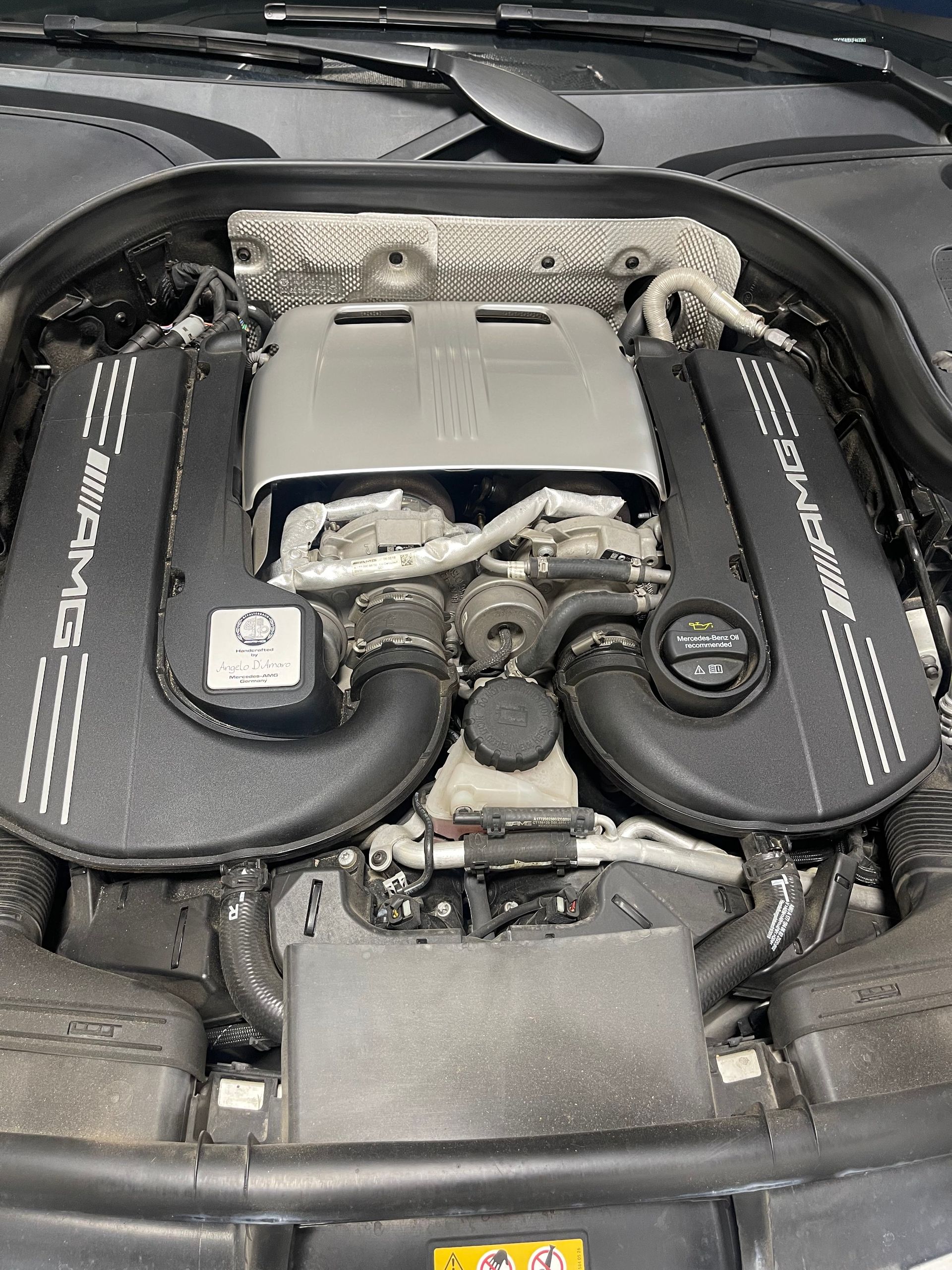 Engine bay of a black Mercedes-AMG car with AMG-branded covers and central components visible. | Benz Tech