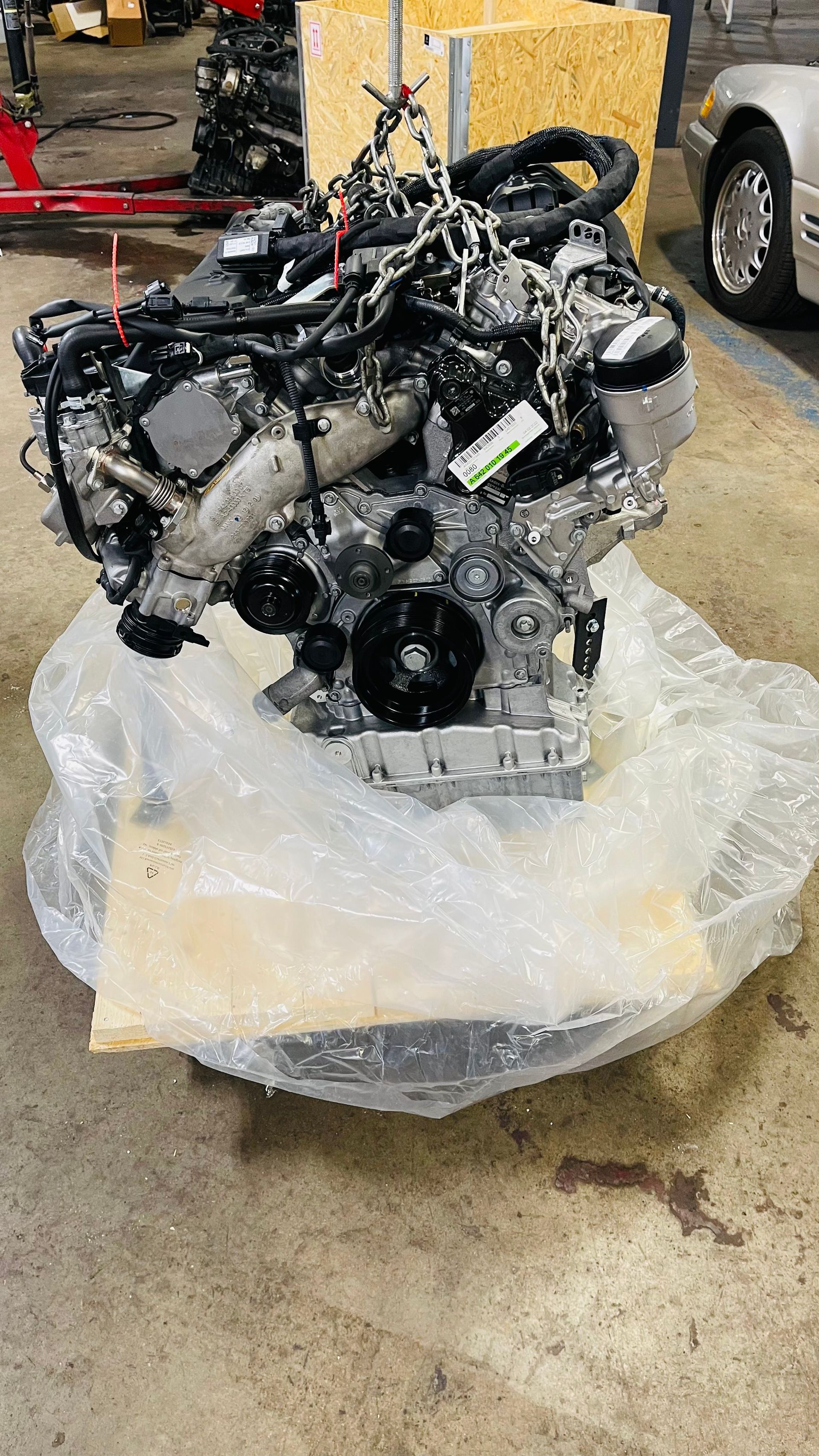 Engine suspended by chains, wrapped in plastic on a garage floor. | Benz Tech