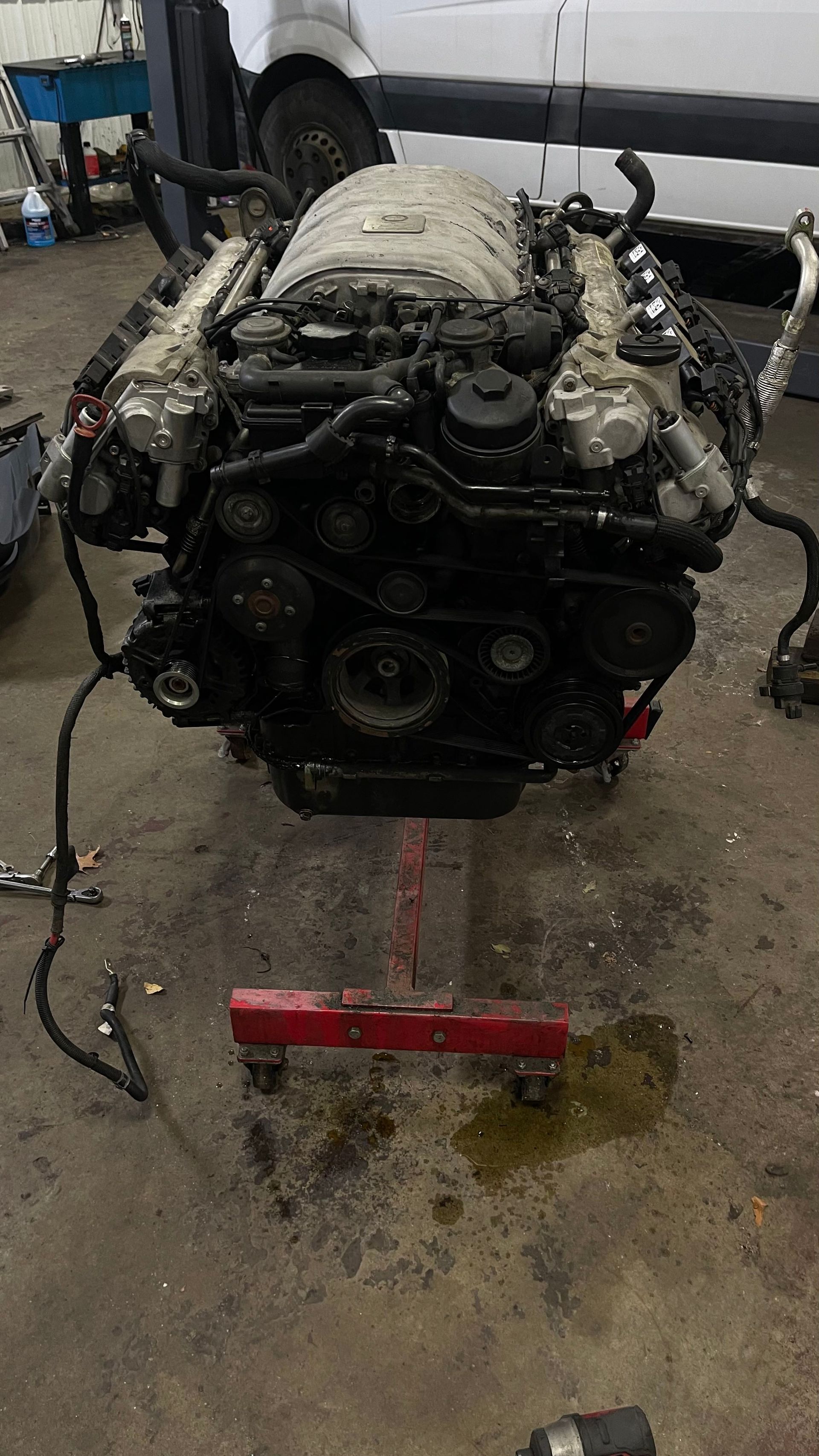 A large, dark engine on a red stand in a garage, possibly being worked on. | Benz Tech