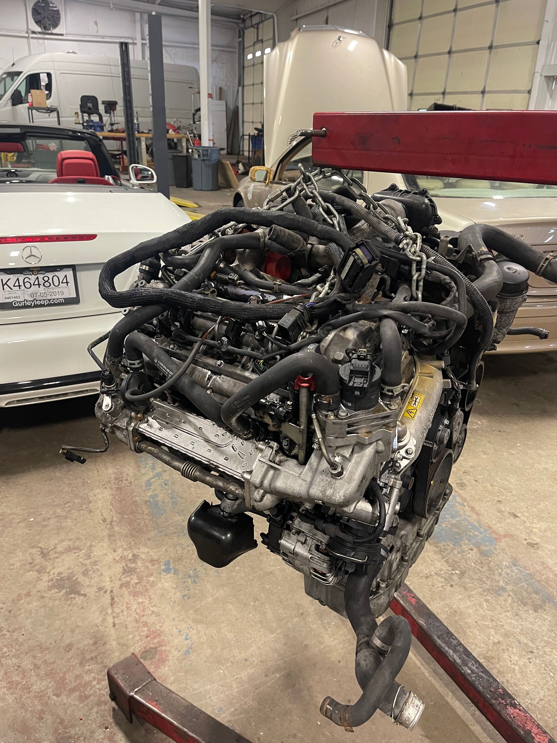 Engine suspended in a garage, entangled with black hoses and wires. | Benz Tech