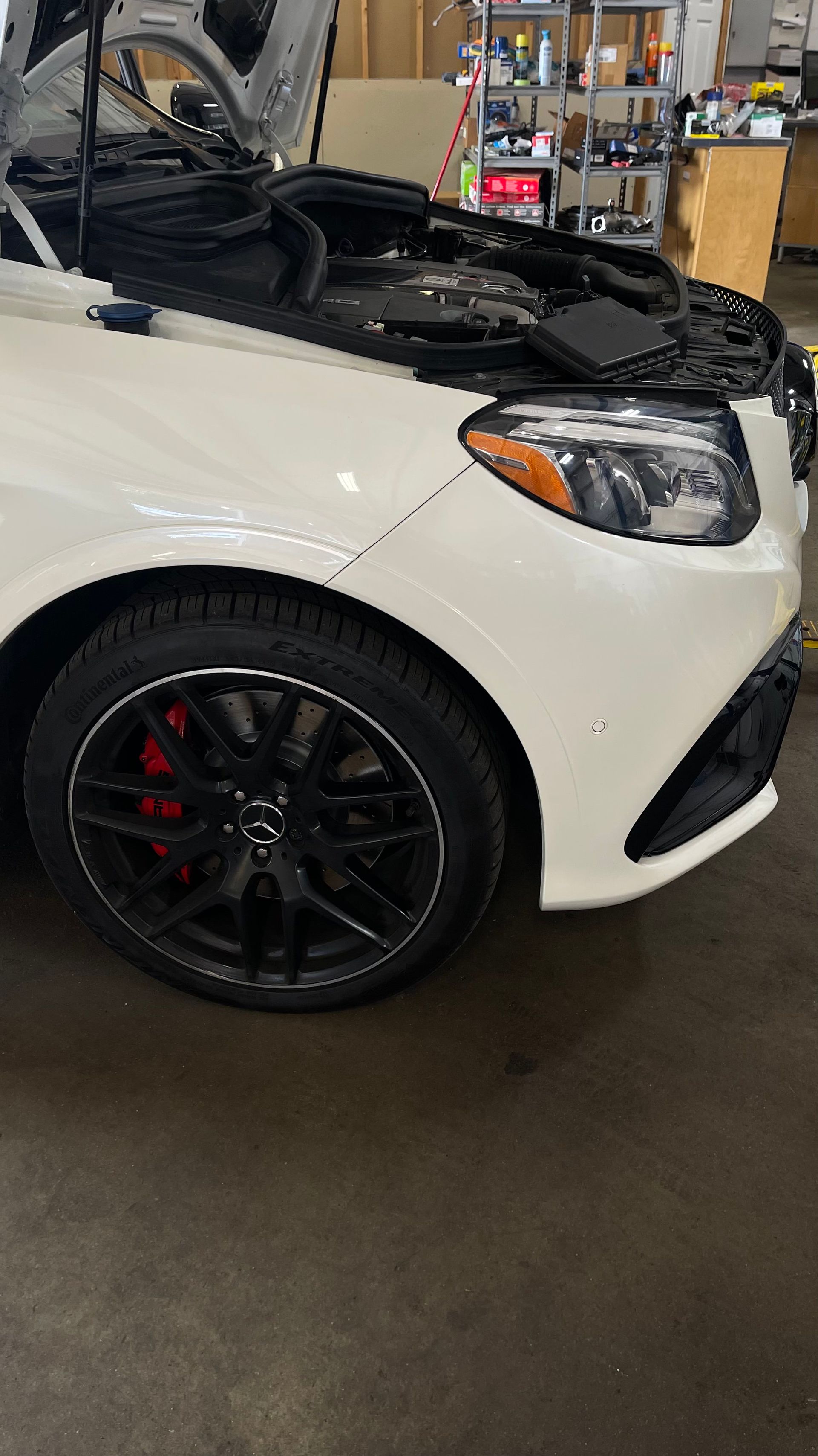 White car with hood open, black rims, red brake calipers, in a garage. | Benz Tech