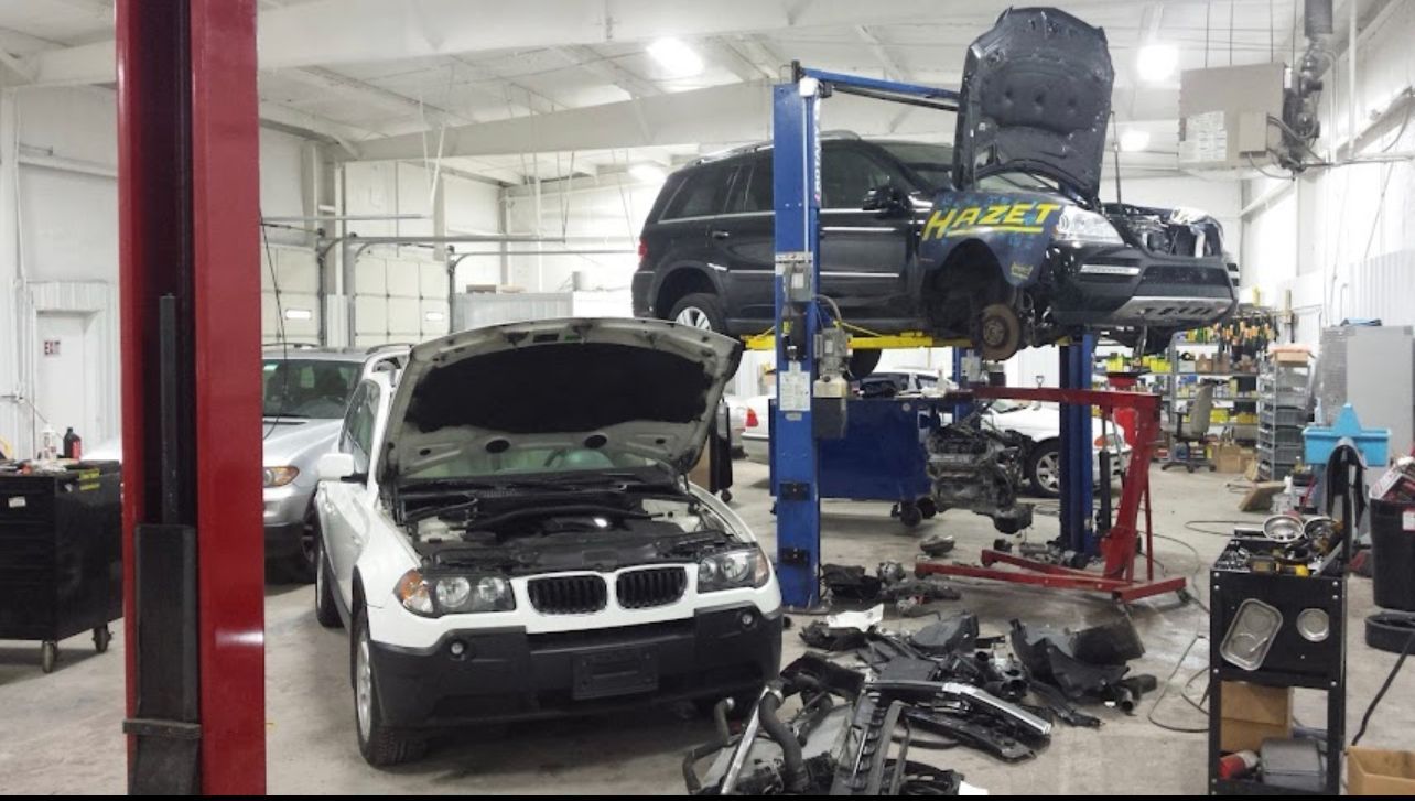 Car repair shop with vehicles on lifts, parts strewn about. White and black SUVs being worked on. | Benz Tech