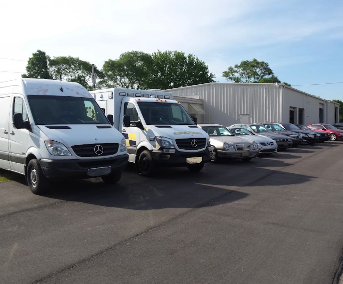 White vans and several cars parked outside a white building on a sunny day. | Benz Tech