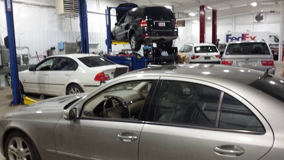 Cars being worked on in a repair shop with lifts; a FedEx van in the background. | Benz Tech