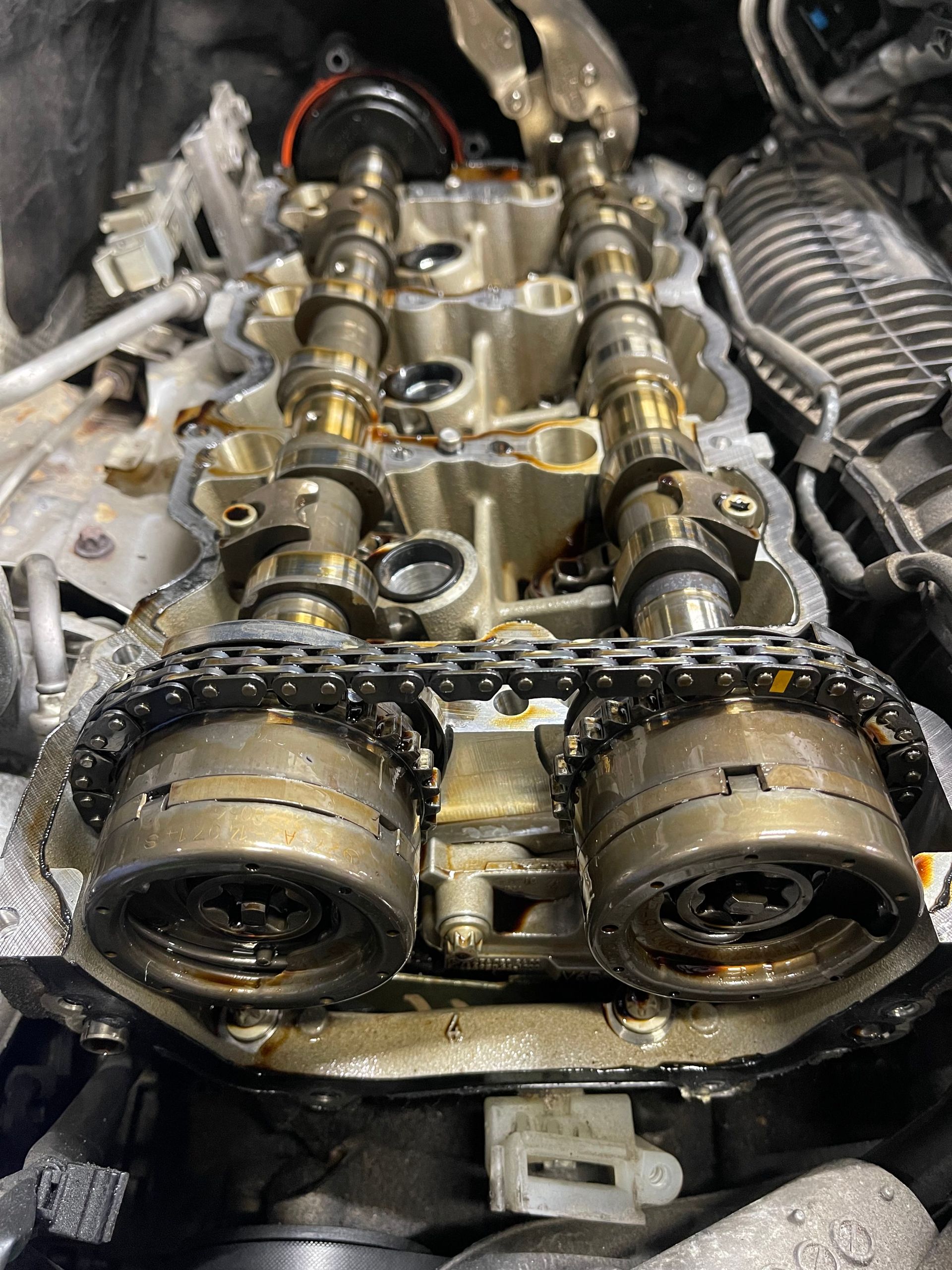 Engine top with visible camshafts, chain, and oil, likely during repair or maintenance. | Benz Tech