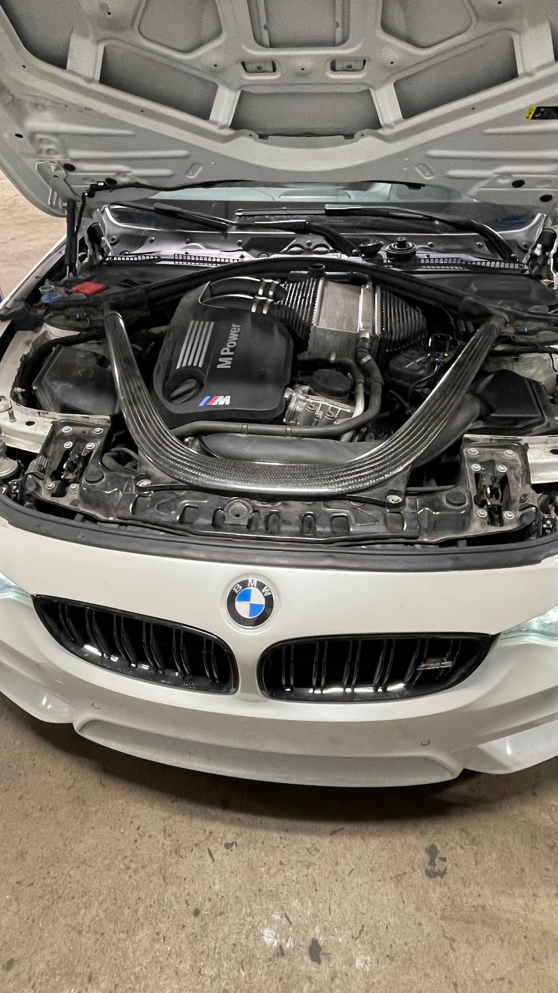 White BMW engine bay with carbon fiber brace, hood open. | Benz Tech