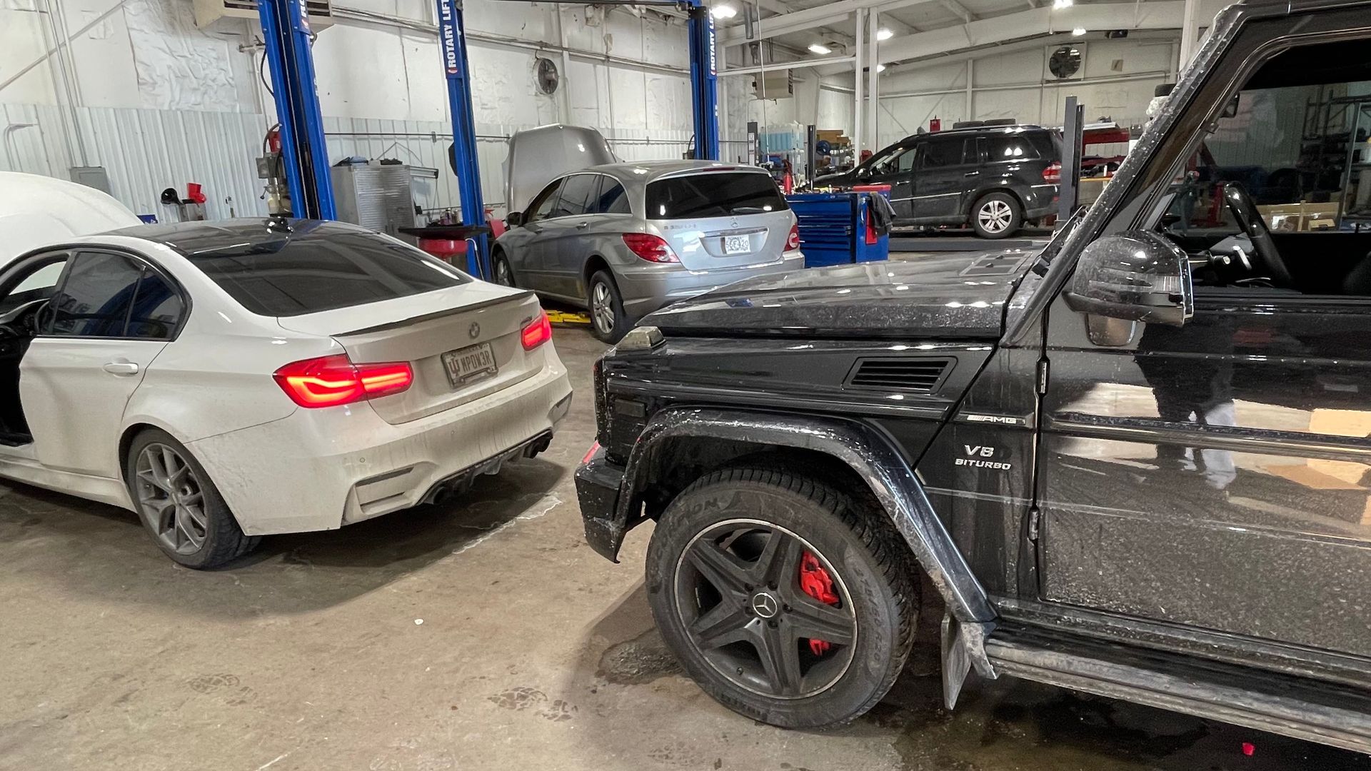 Black SUV and white car inside auto repair shop. | Benz Tech
