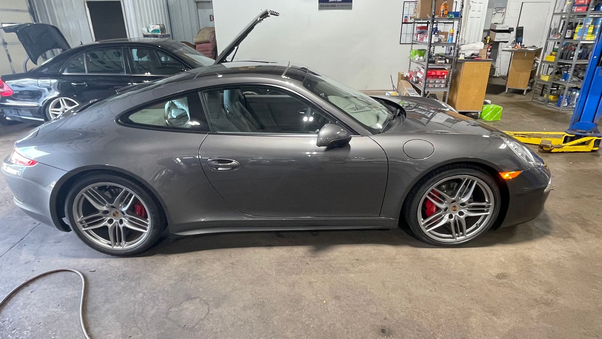 Gray Porsche sports car parked in a garage, with a black car in the background. | Benz Tech