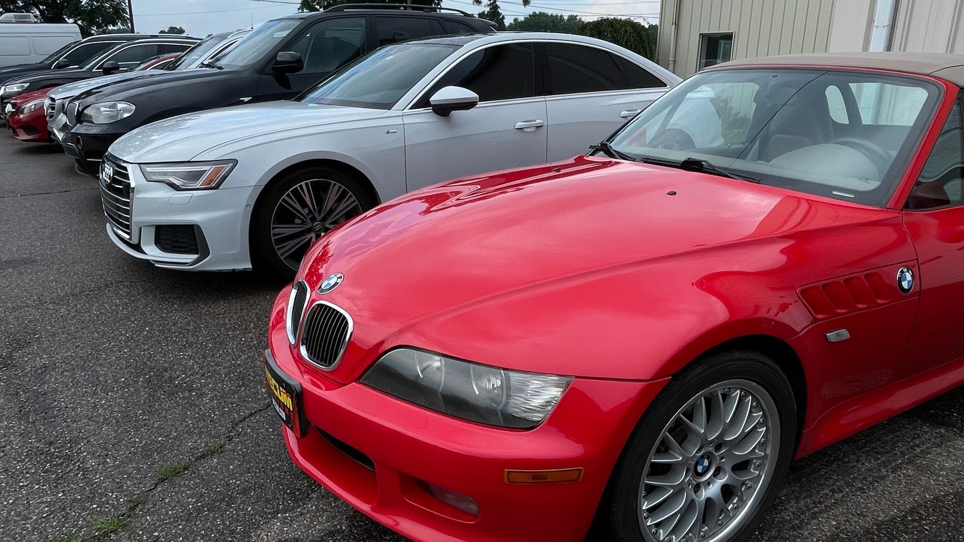 Red BMW convertible parked in a lot with other cars, including a white Audi. | Benz Tech