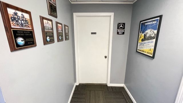 Narrow hallway with awards, a white door, and a poster. Gray walls, dark floor. | Benz Tech